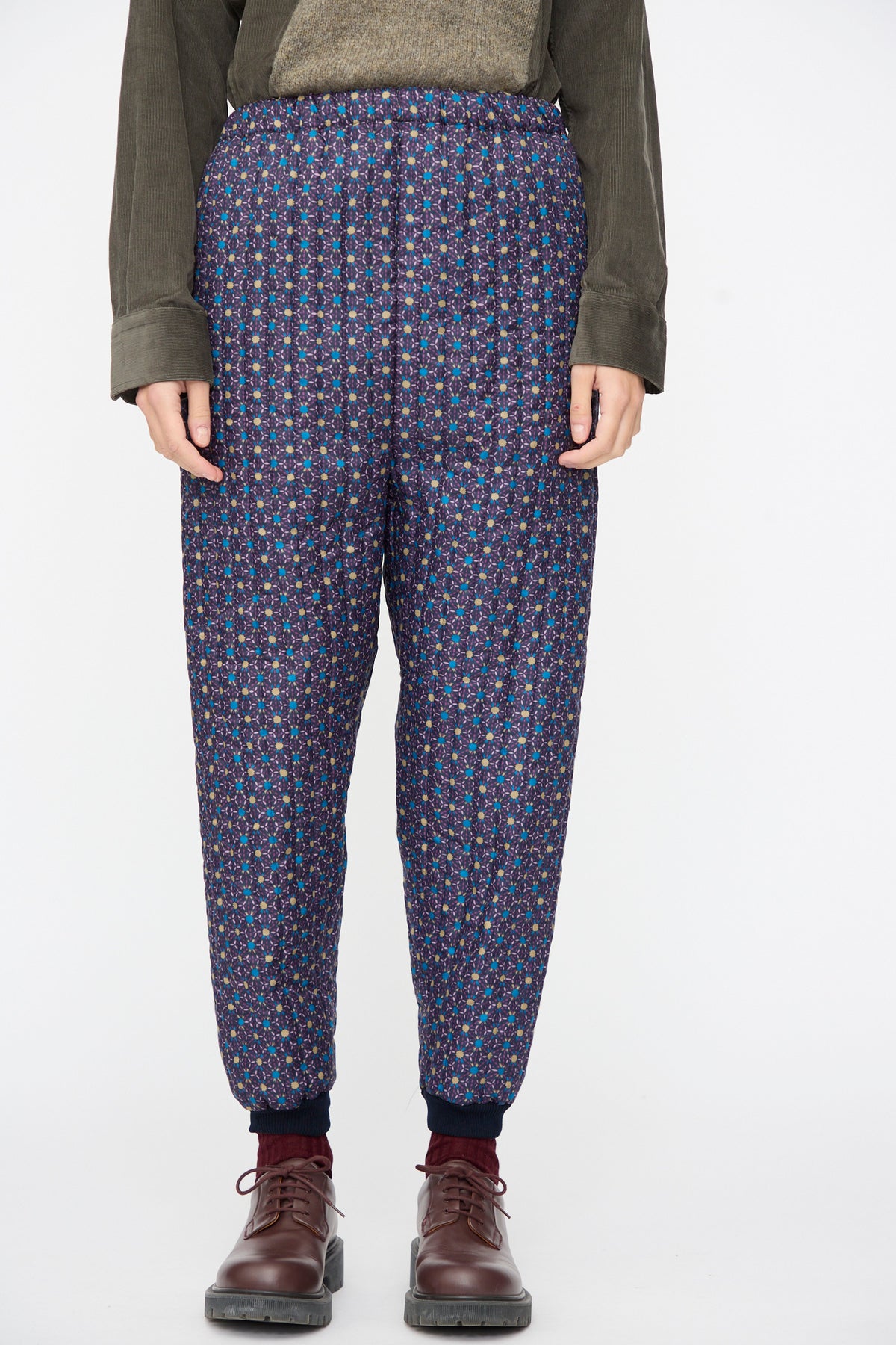 Person wearing dark blue Bless No. 08 Monpe Pants in Floral Print II with a small geometric floral pattern and dark cuffs, paired with brown leather shoes.