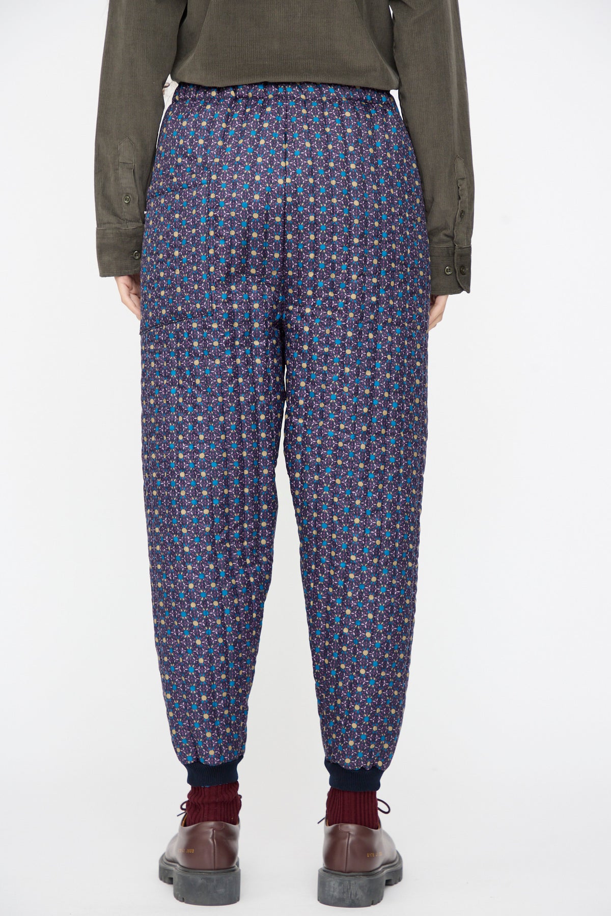 Back view of Bless No. 08 Monpe Pants in Floral Print II, featuring a tapered fit, purple, blue, and yellow geometric floral print, and a dark blue ribbed ankle cuff.