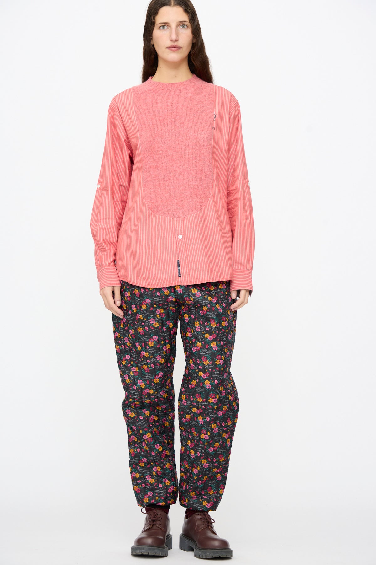 A person wearing a pink striped shirt with a textured chest panel, Bless No. 08 Monpe Pants in Floral Print IV, and dark brown shoes.