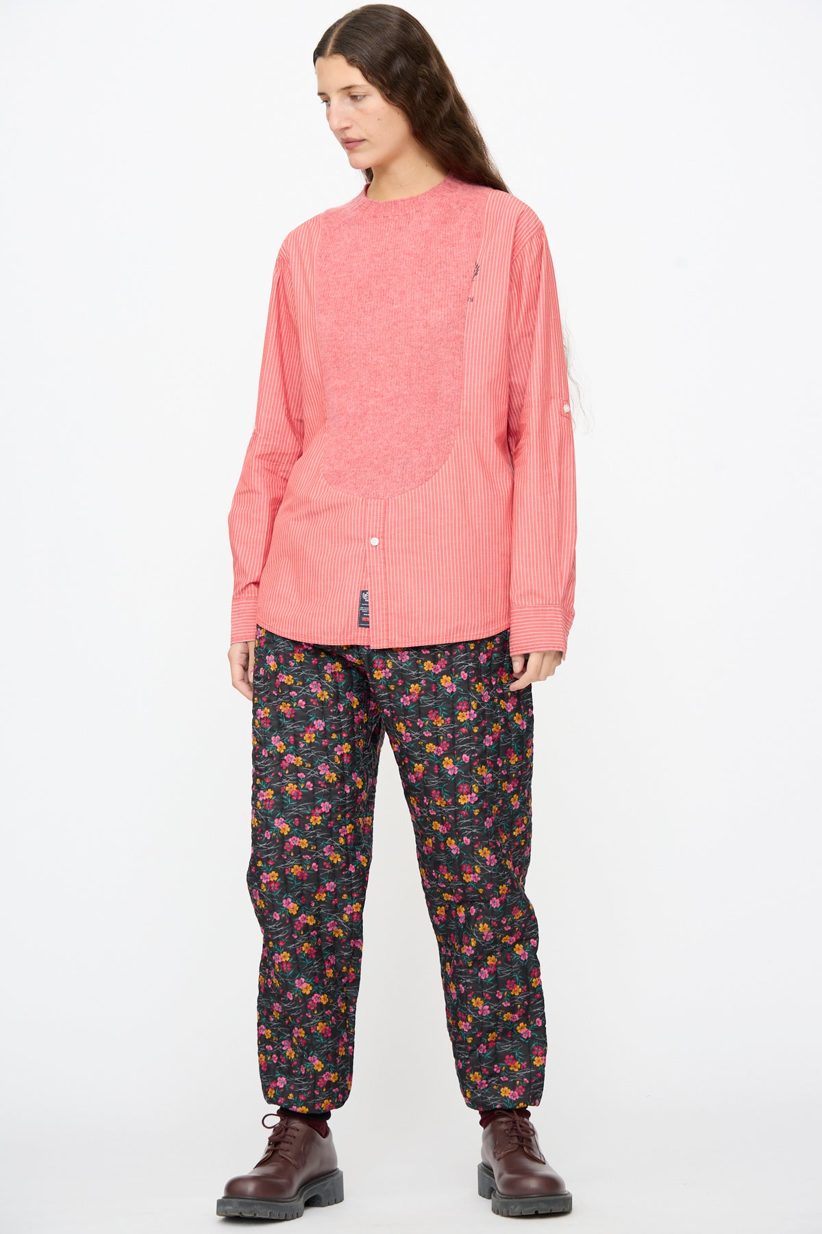 A person wears a pink striped shirt with a textured chest panel and Bless No. 08 Monpe Pants in Floral Print IV, paired with dark brown boots.