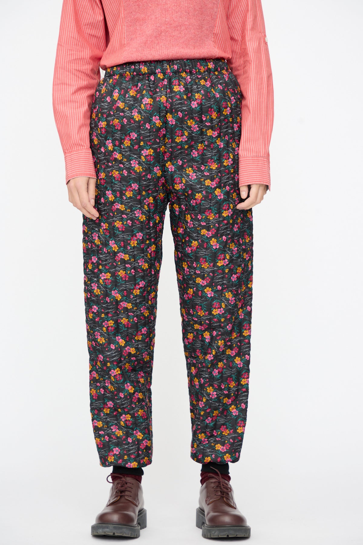 Bless No. 08 Monpe Pants in Floral Print IV, featuring a relaxed-fit black floral nylon fabric, worn with a pink striped shirt and brown lace-up shoes.