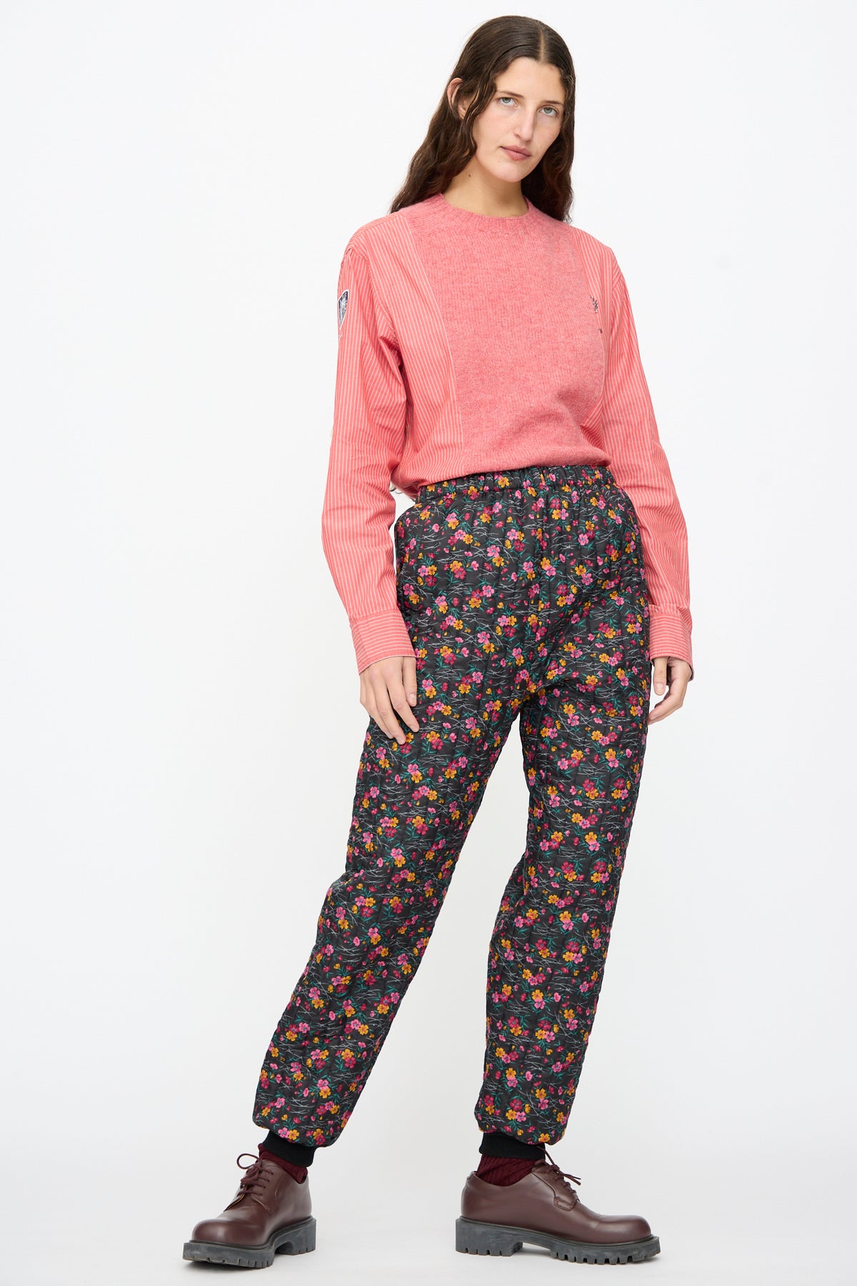 A person wearing a long-sleeved red shirt and Bless No. 08 Monpe Pants in Floral Print IV, paired with brown lace-up shoes.