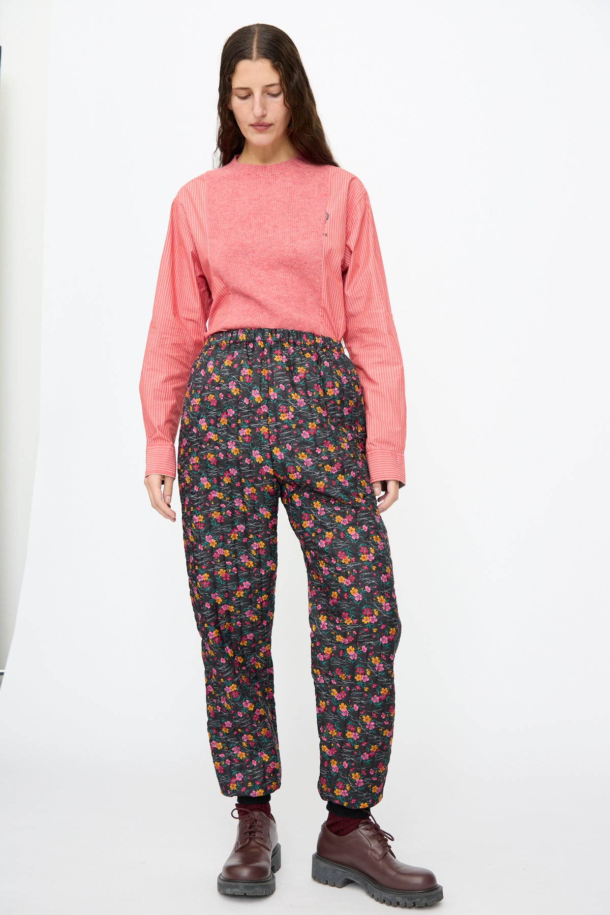 A person wears a pink long-sleeved shirt tucked into Bless No. 08 Monpe Pants in Floral Print IV and dark brown lace-up boots.