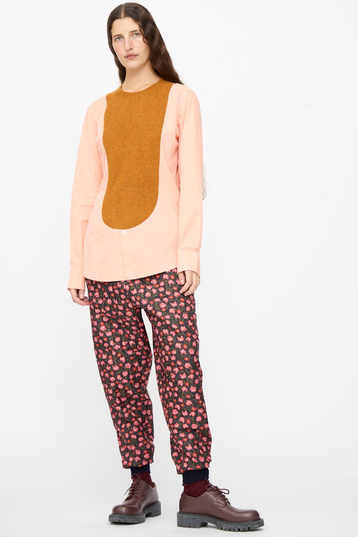 A person wears a light pink button-down shirt with a brown front panel, Bless No. 08 Monpe Pants in Floral Print V, and brown lace-up shoes.