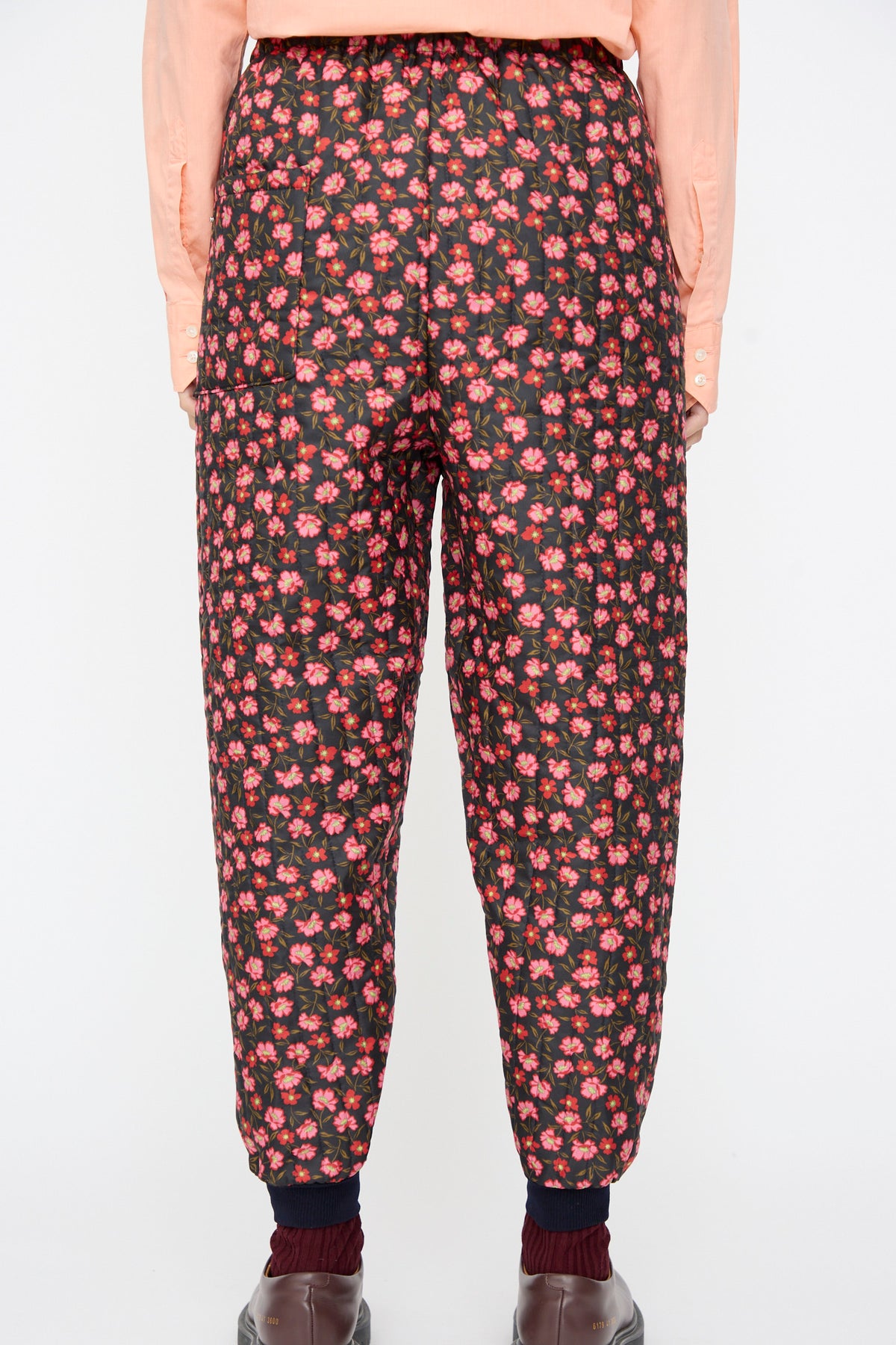 A person wearing No. 08 Monpe Pants in Floral Print V, styled with a peach-colored shirt and dark shoes.