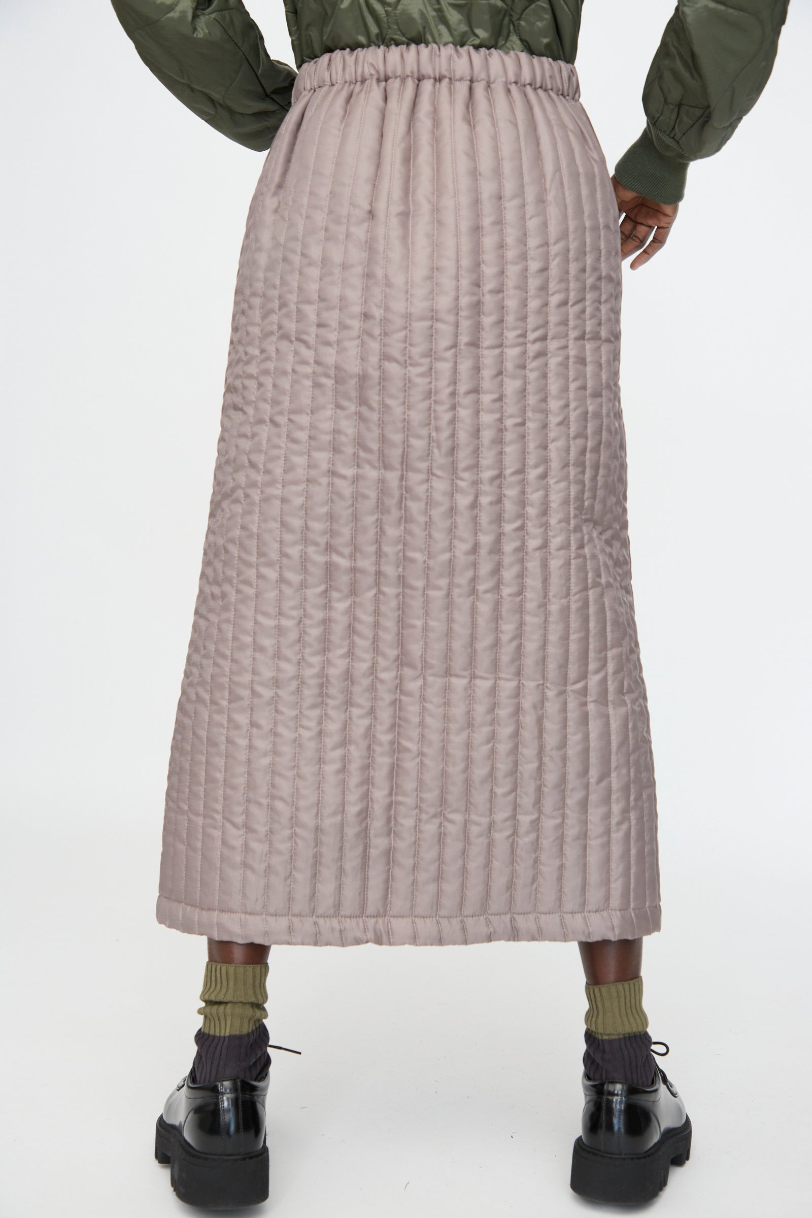 A person is shown from the back wearing the Bless No. 08 Monpe Skirt in Beige, paired with a green jacket, olive socks, and black shoes, set against a plain background.