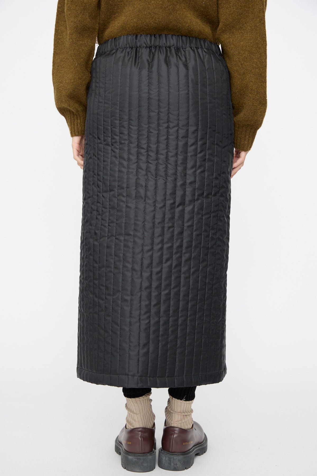 Back view of a person wearing a black No. 08 Monpe Skirt, a long quilted nylon midi skirt with an elastic waistband.