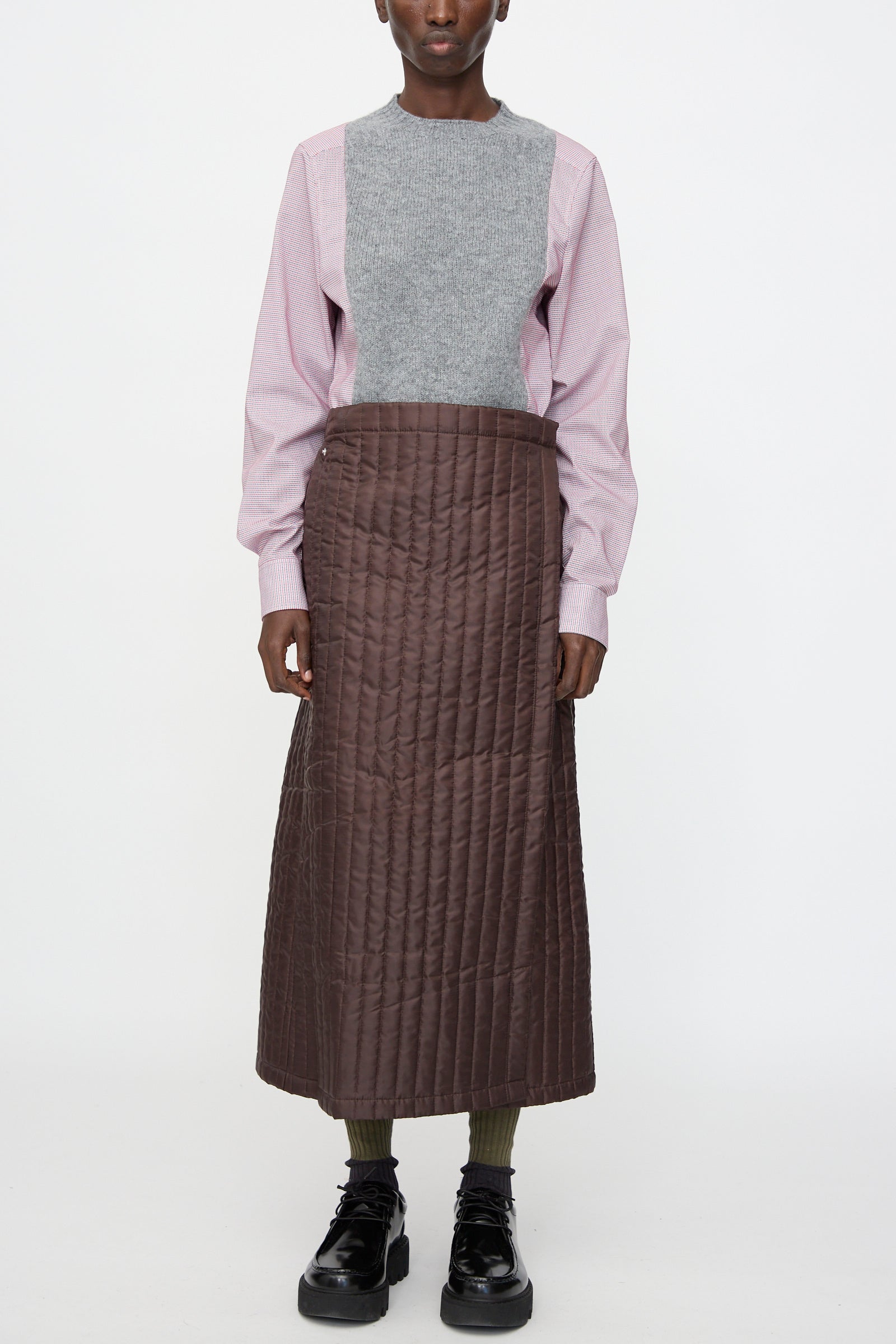 A person wearing a grey and pink long-sleeve shirt, the Bless No. 08 Monpe Skirt in Brown, green socks, and black platform shoes stands against a plain white background.