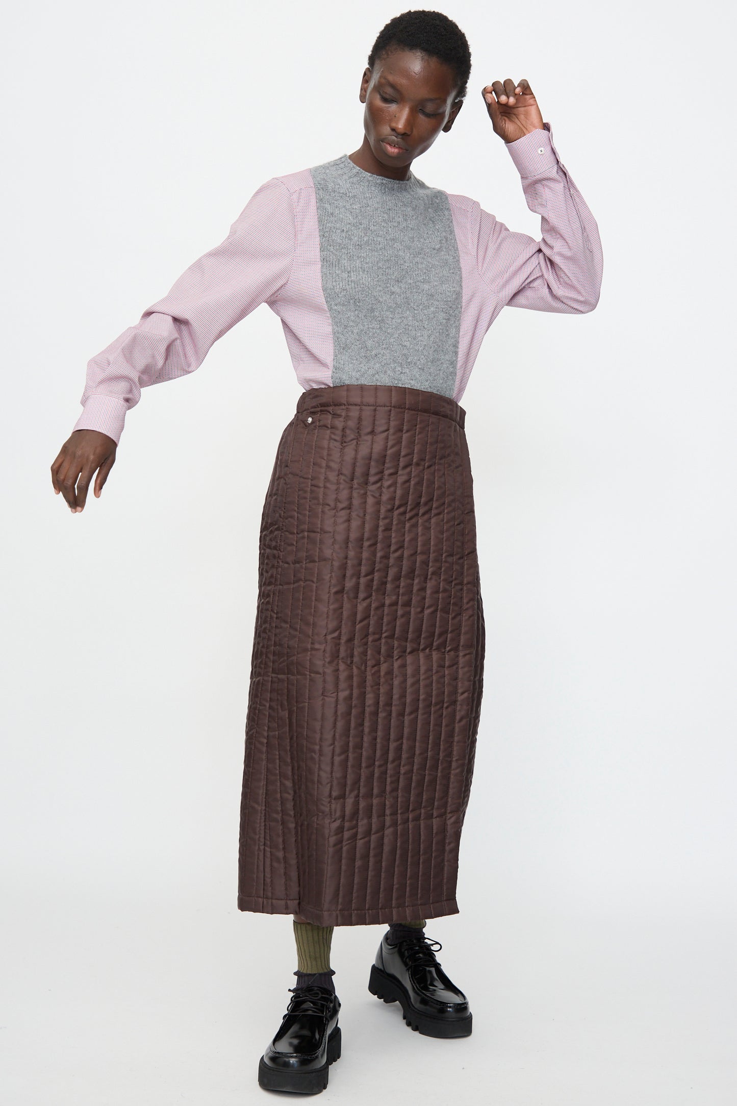 A person wears the Bless No. 08 Monpe Skirt in Brown, paired with a gray and pink color-blocked sweater, olive-green socks, and black platform shoes, standing against a plain white background.
