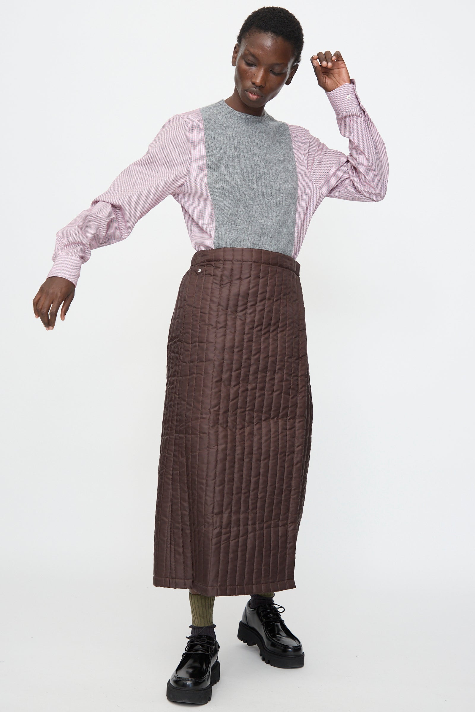 A person wears the Bless No. 08 Monpe Skirt in Brown, paired with a gray and pink color-blocked sweater, olive-green socks, and black platform shoes, standing against a plain white background.