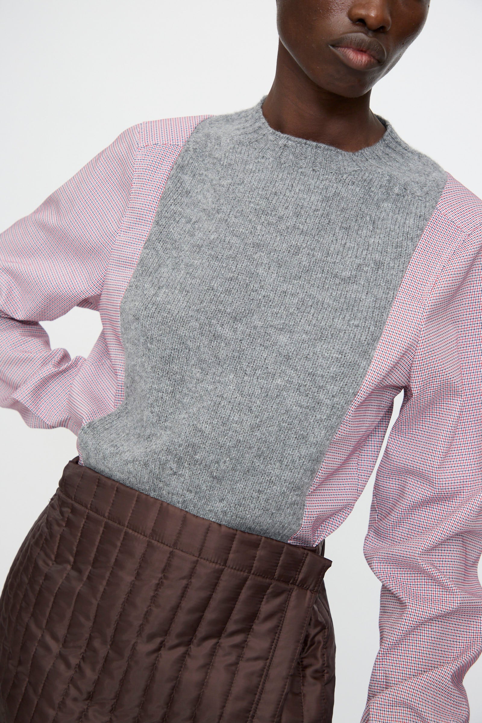 A person wears the Bless No. 08 Monpe Skirt in Brown, styled with a gray knit vest over a red checkered shirt, photographed from shoulders to waist.
