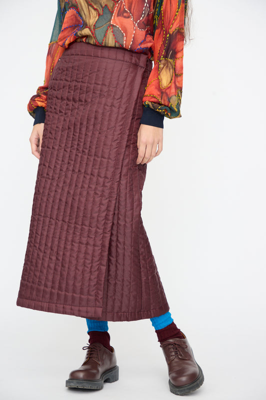 A person wears a Bless No. 08 Monpe Skirt in Burgundy over blue leggings and dark brown lace-up shoes.