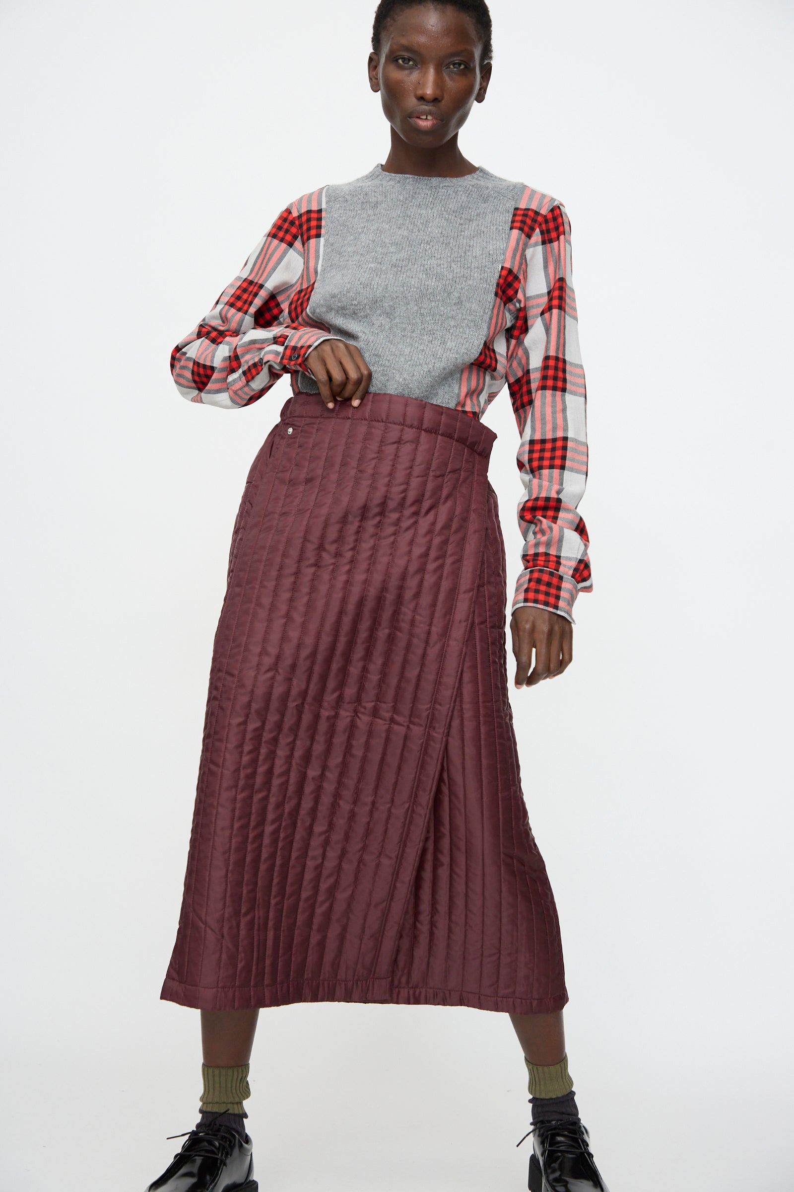A person wearing a gray sleeveless top over a red plaid shirt and the Bless No. 08 Monpe Skirt in Burgundy, standing against a plain white background.