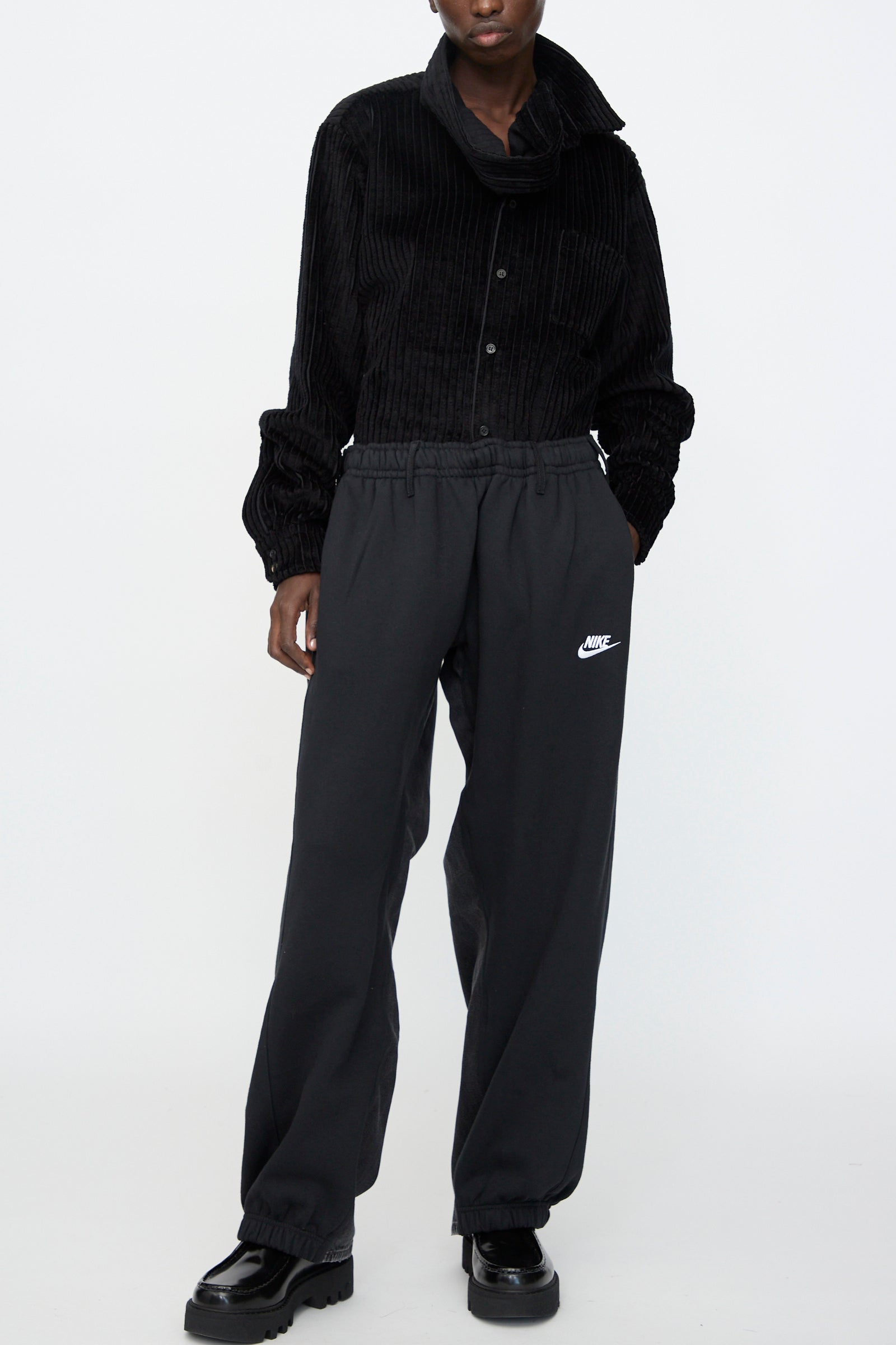 A person wearing a black textured button-up shirt, Bless No. 61 Overjoggingjeans in Black, and black platform shoes, standing against a plain white background.