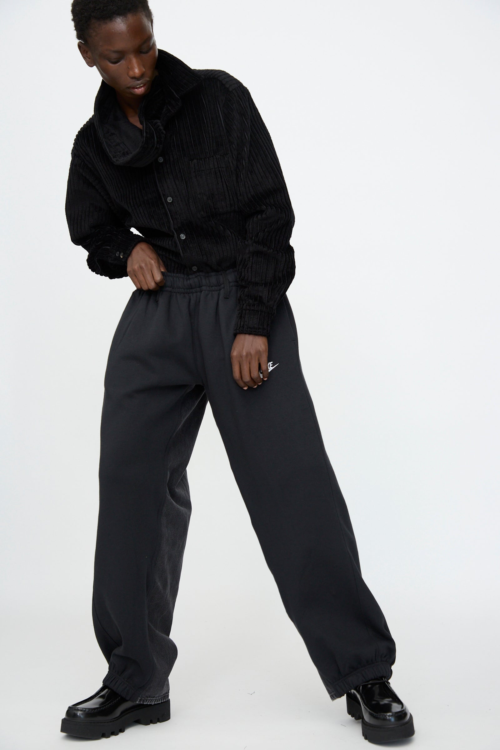 Person wearing a black corduroy jacket, Bless No. 61 Overjoggingjeans in Black, and black shoes, standing against a plain white background.