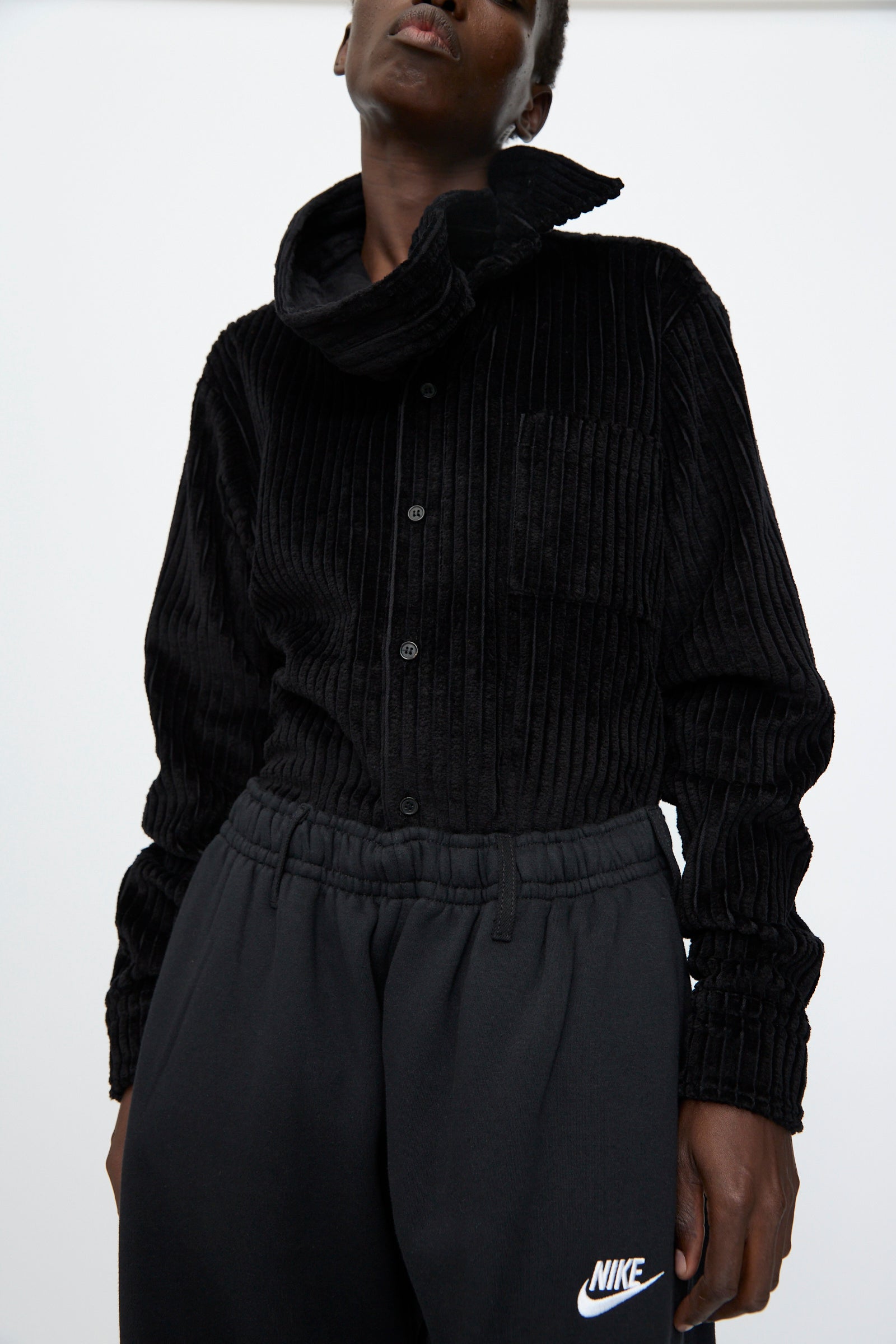 Person wearing a black corduroy button-up shirt and Bless No. 61 Overjoggingjeans in Black with an oversized fit, standing against a plain light background.