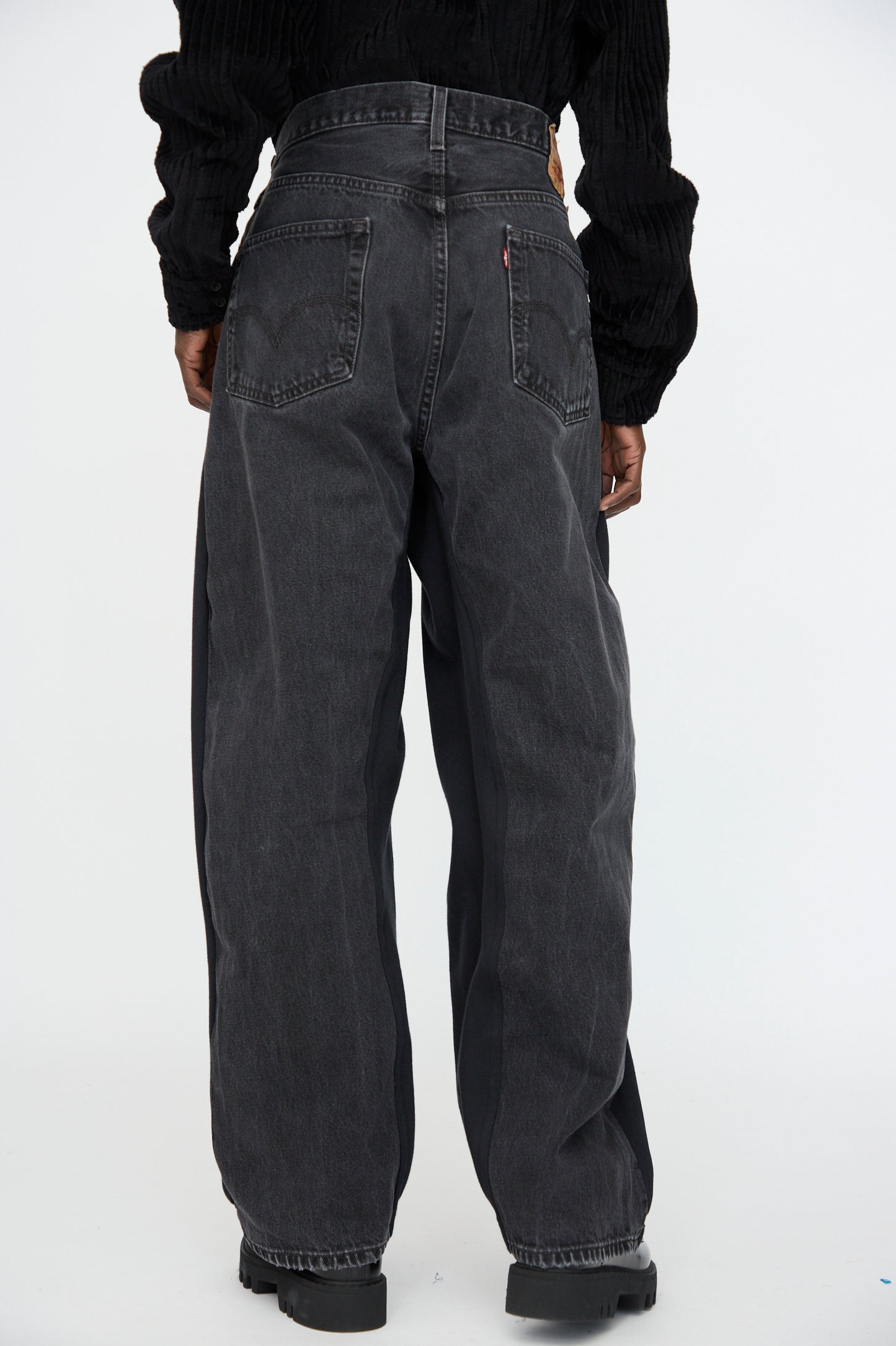 A person wearing Bless No. 61 Overjoggingjeans in Black and black shoes stands with their back to the camera against a plain white background.