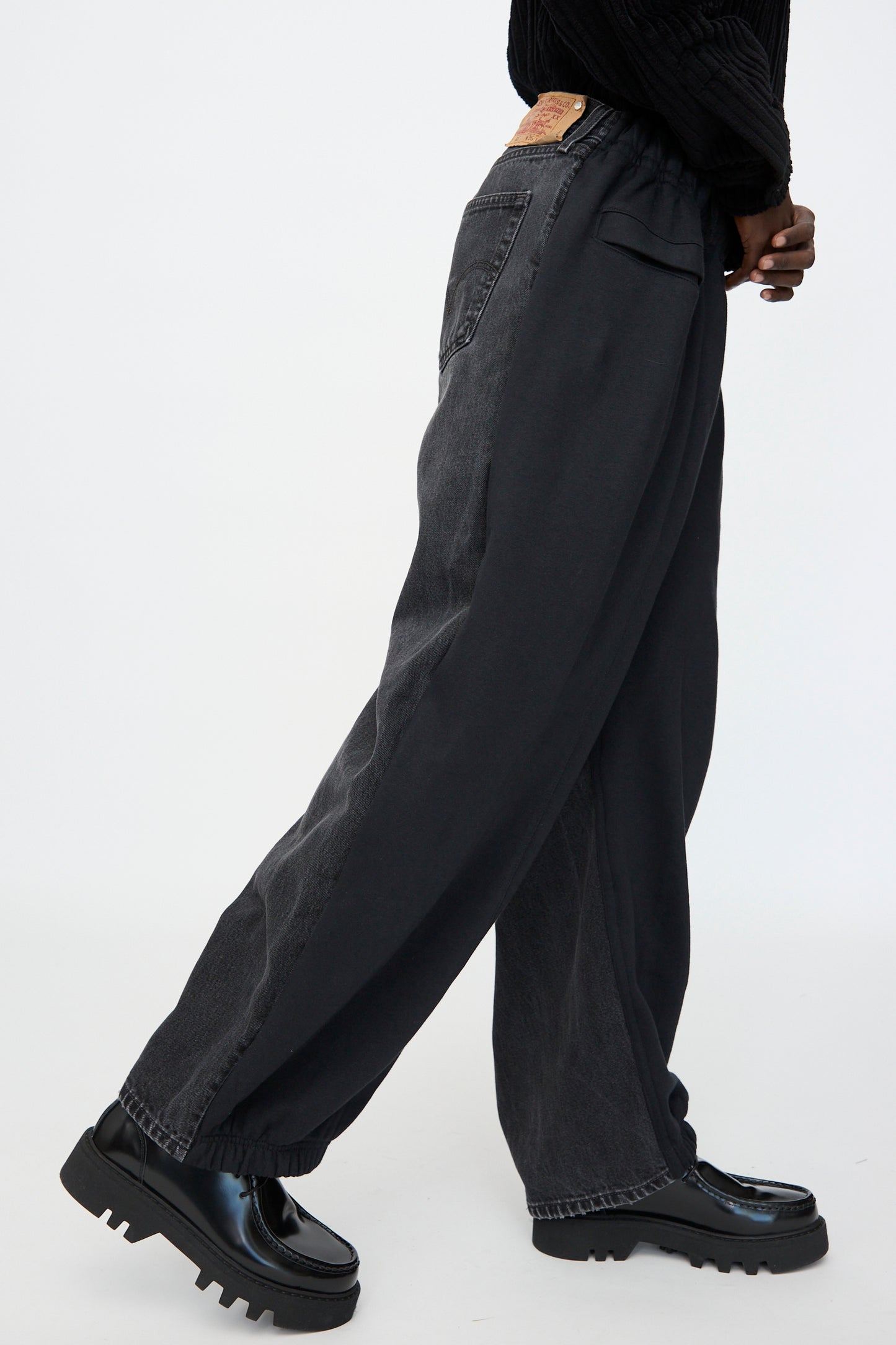 Model wearing Bless No. 61 Overjoggingjeans in Black with shiny black platform shoes, photographed from the side against a plain background.