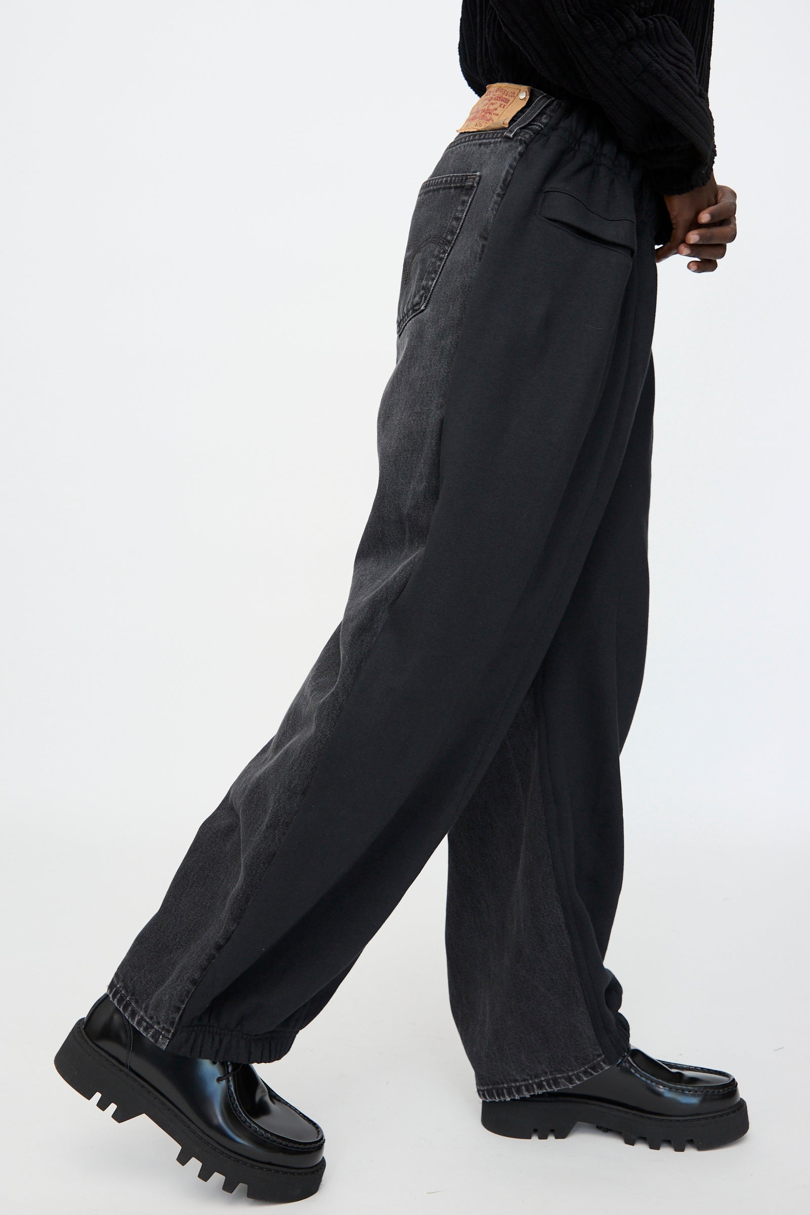 Model wearing Bless No. 61 Overjoggingjeans in Black with shiny black platform shoes, photographed from the side against a plain background.