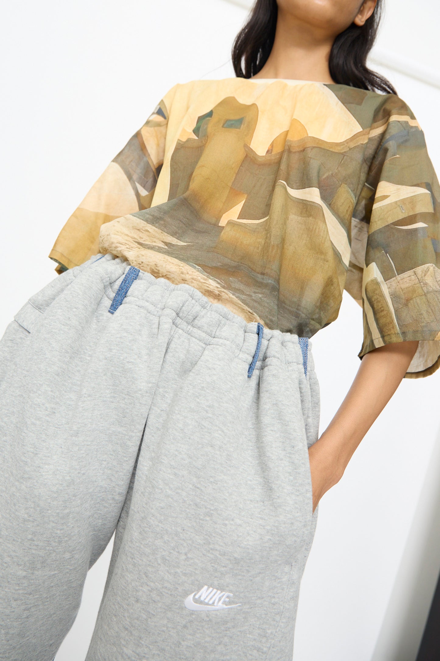 Person wearing a printed shirt with an abstract building design and relaxed fit Bless No. 61 Overjoggingjeans in lightgrey and denimblue, standing against a plain background.