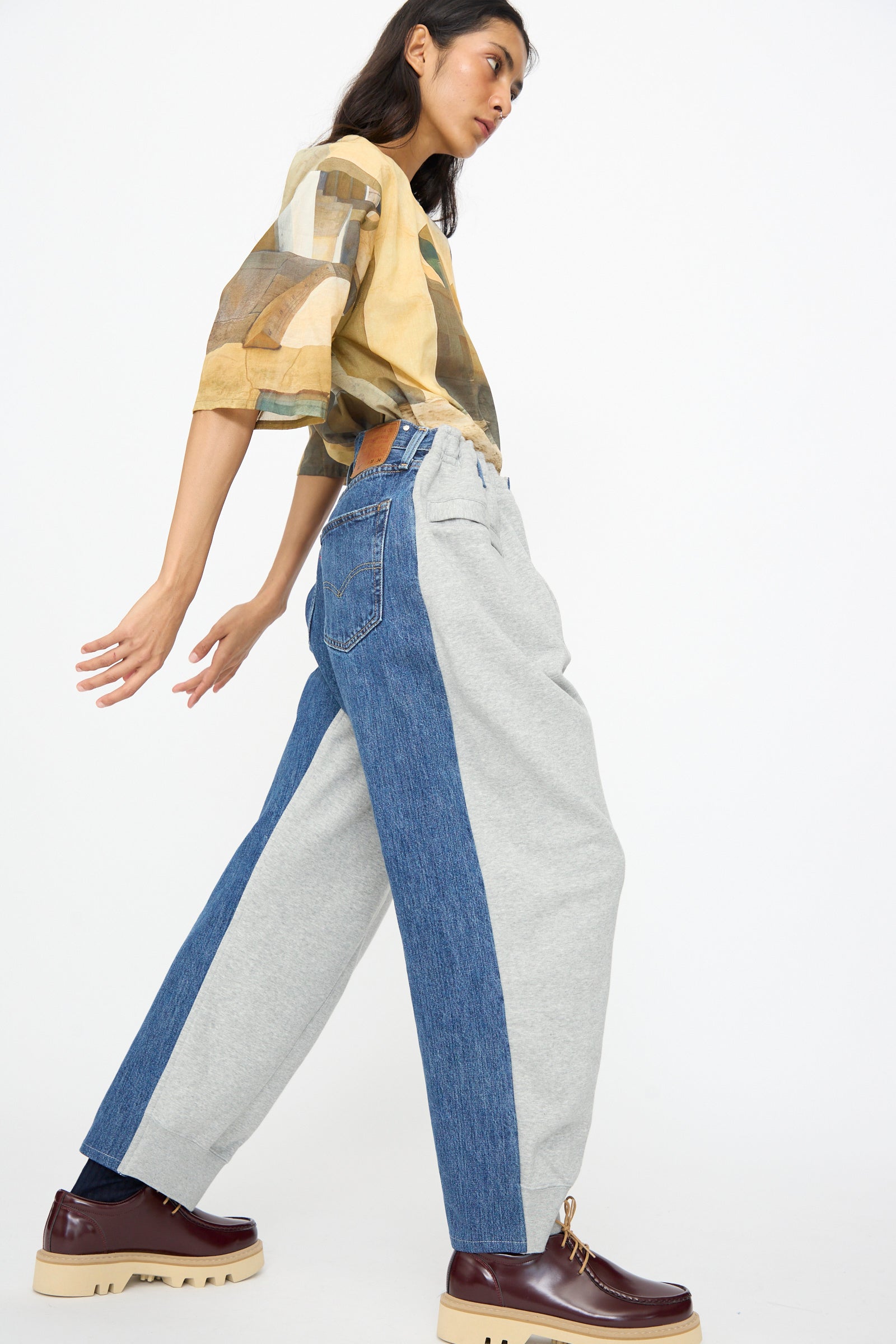 Person walking sideways in a patterned shirt, Bless No. 61 Overjoggingjeans in Lightgrey and Denimblue, and platform brown shoes against a plain white background.