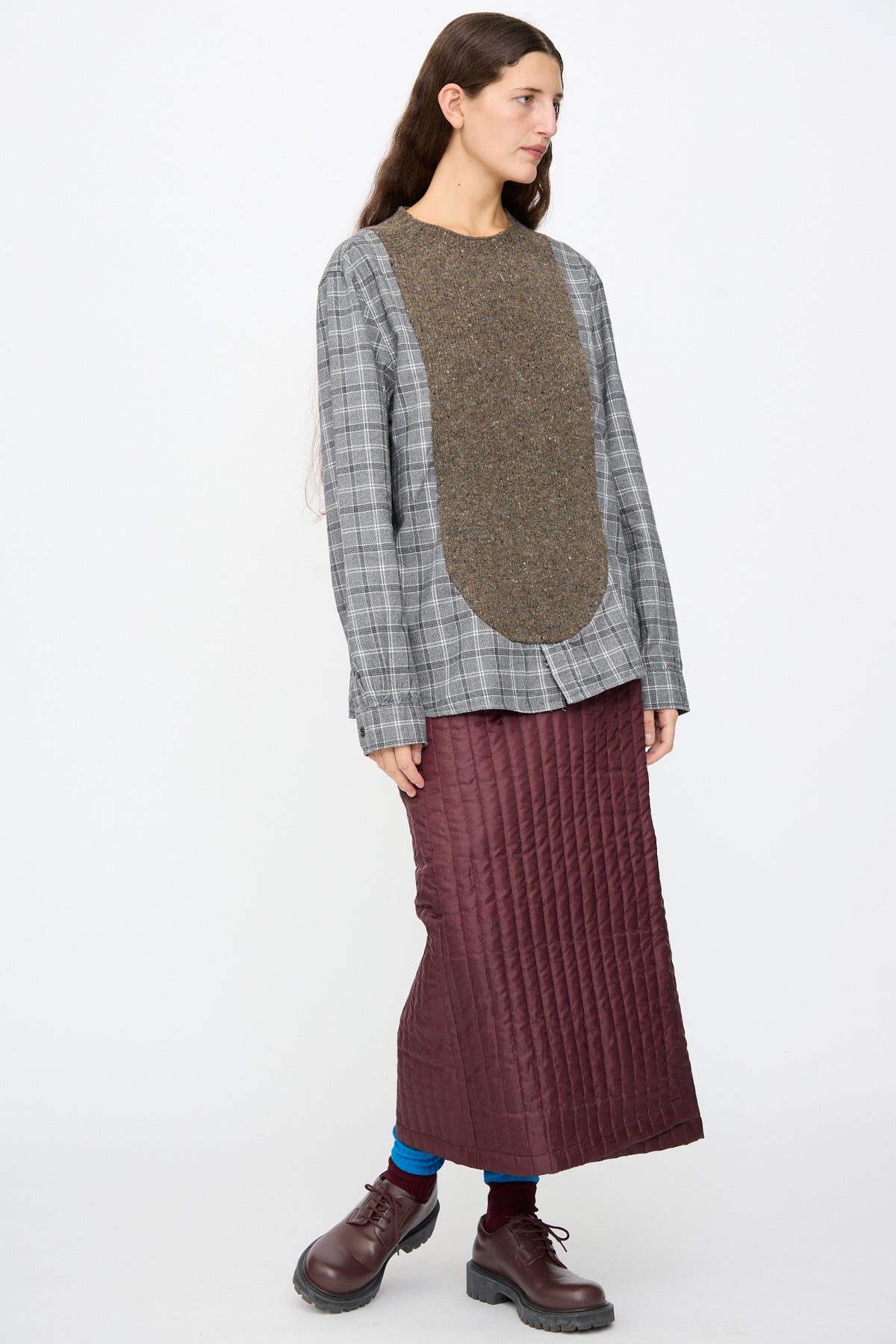 A person wearing a Bless No. 68 Frontinsertpullover in Unique I with a brown textured chest panel, a long quilted maroon skirt, and dark brown lace-up shoes.