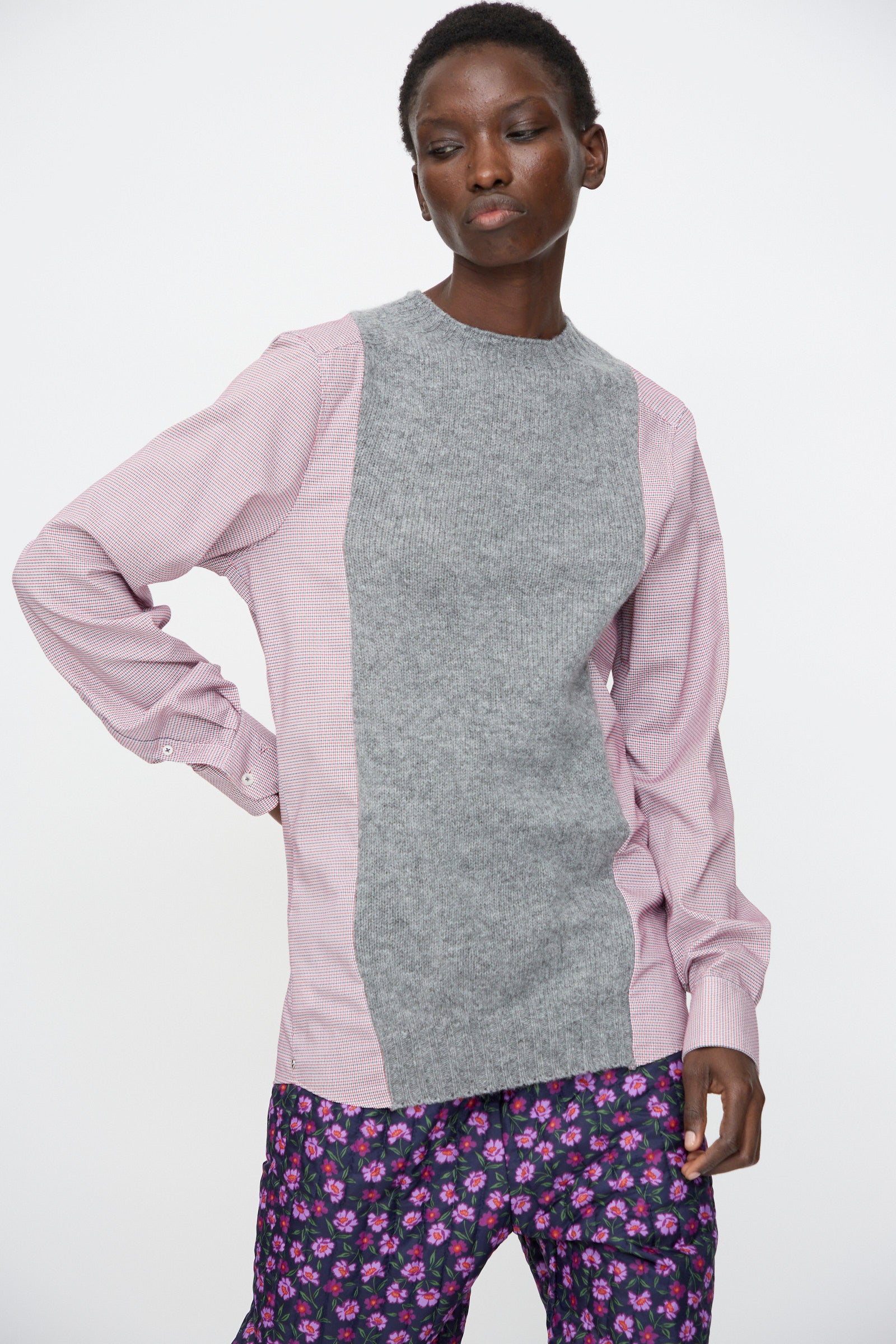 A person wears the Bless No. 68 Frontinsertpullover in Unique I, featuring light pink sleeves and a gray Shetland wool panel, paired with purple floral pants, standing against a plain white background.