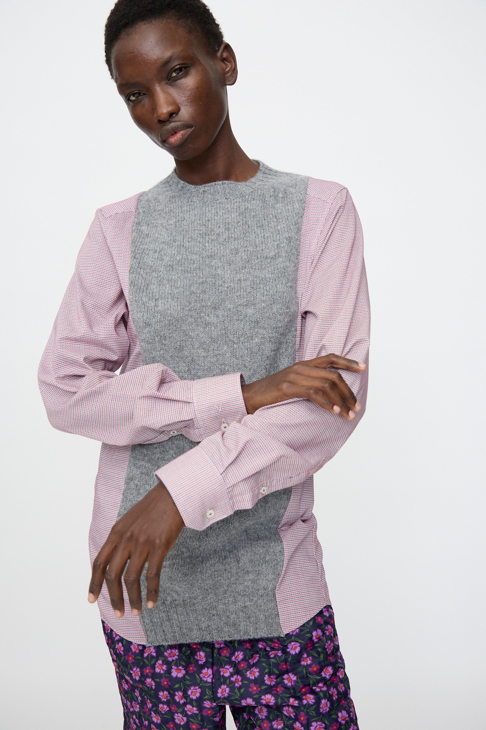A person wears the Bless No. 68 Frontinsertpullover in Unique I, featuring a cotton poplin shirt with shetland wool panel and pink striped sleeves, paired with purple floral pants, standing against a plain white background.