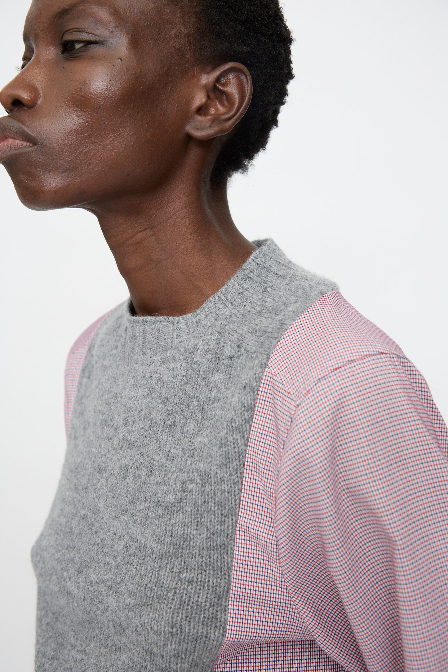 A person wears the Bless No. 68 Frontinsertpullover in Unique I, a grey shetland wool panel sleeveless sweater, layered over a pink patterned cotton poplin shirt, shown from the side against a plain background.