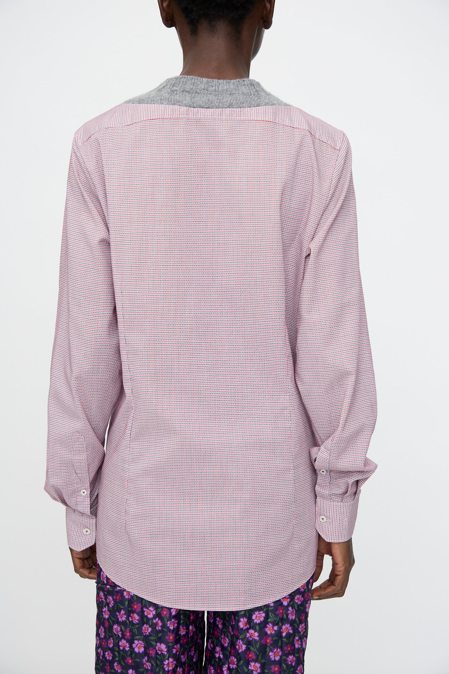 A person is seen from behind wearing the No. 68 Frontinsertpullover in Unique I by Bless—a long-sleeve, light red patterned cotton poplin shirt with a gray collar—paired with floral purple shorts.