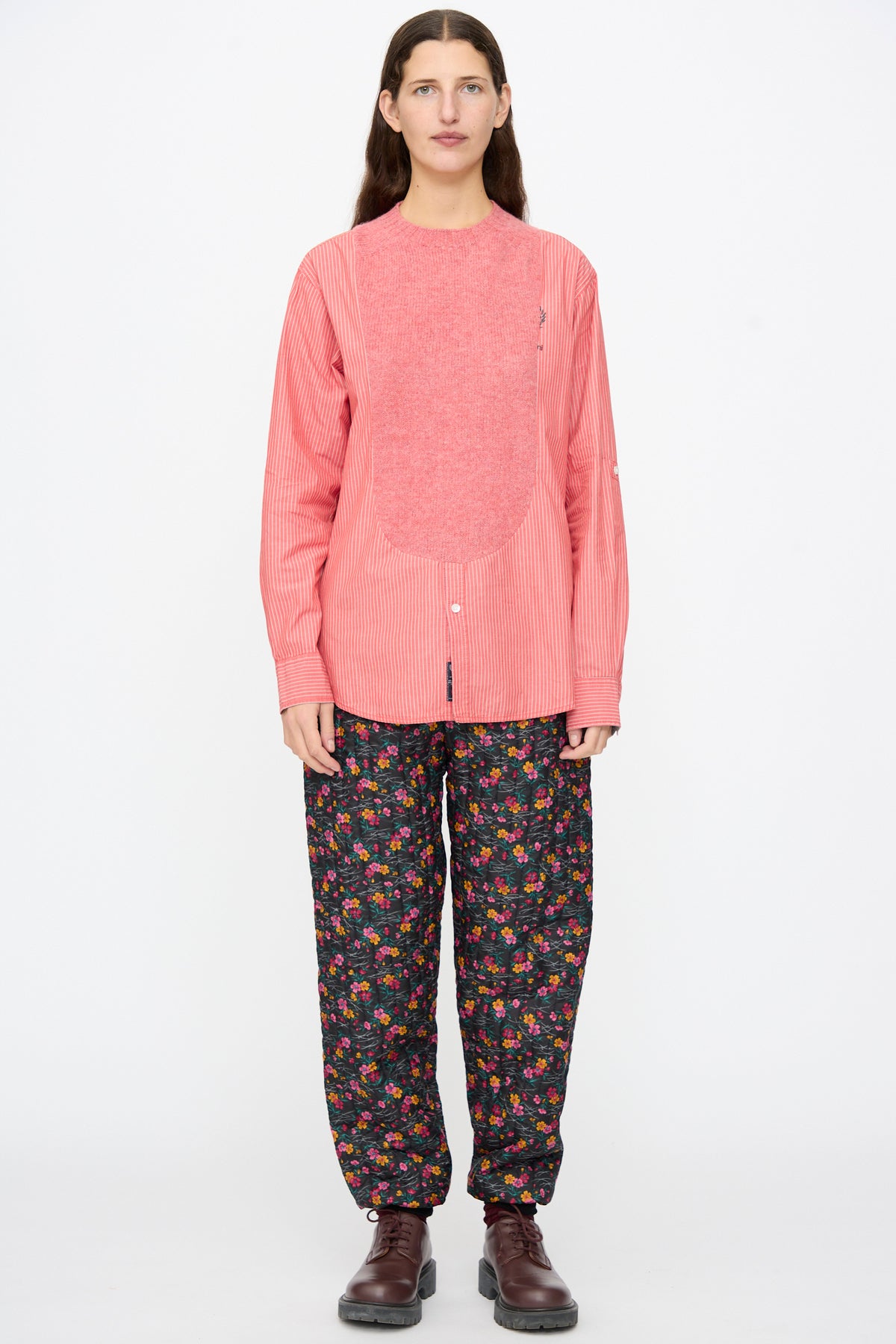 A person wearing a Bless No. 68 Frontinsertpullover in Unique II with a pink textured front panel, paired with dark floral print trousers and brown lace-up shoes.