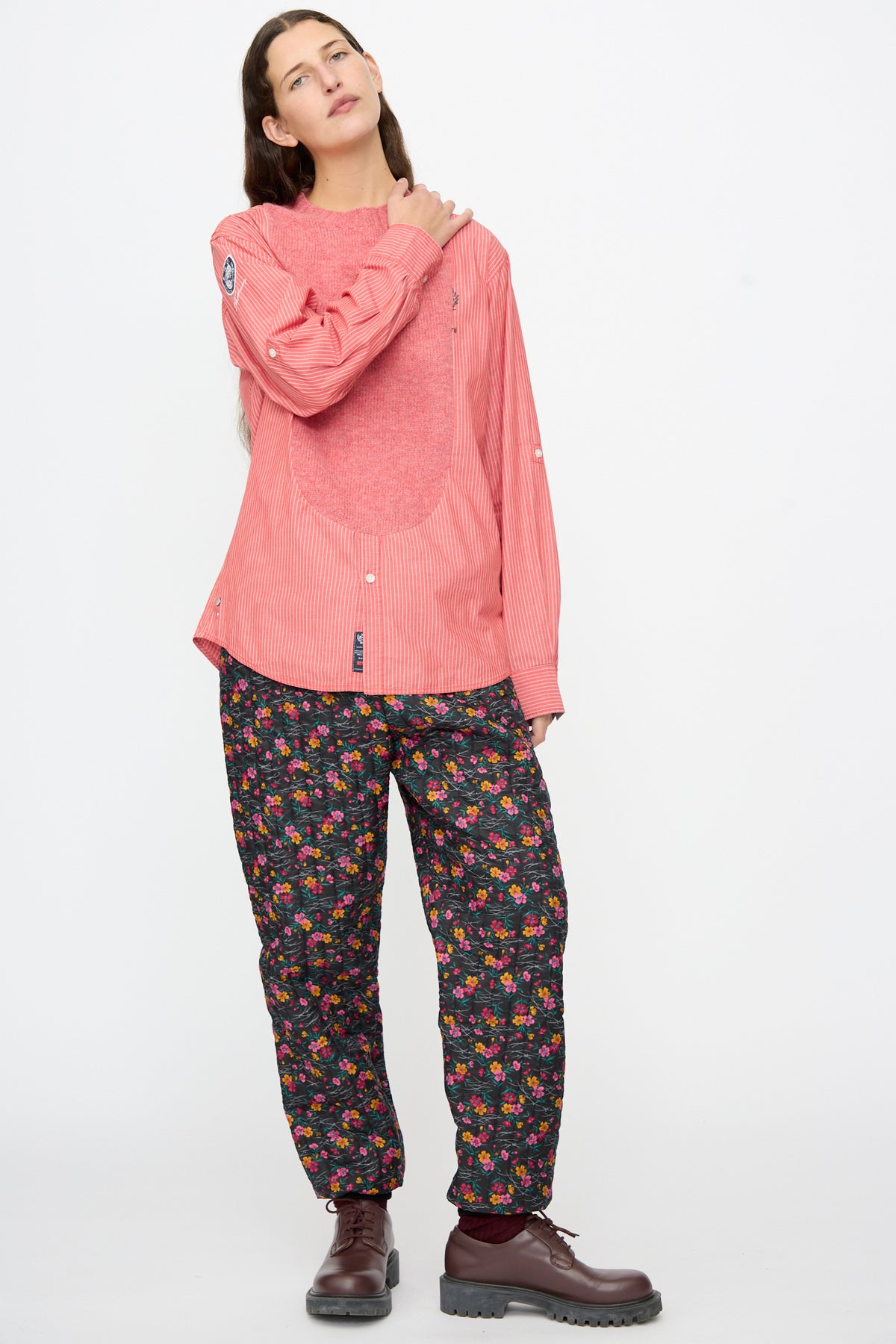 A person wearing a Bless No. 68 Frontinsertpullover in Unique II with a textured chest panel and dark floral-print pants, paired with brown leather boots.