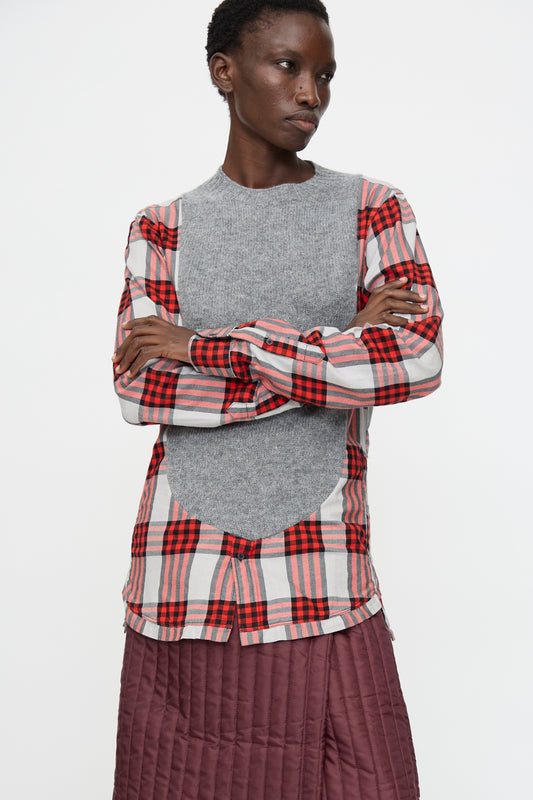 A person stands with arms crossed wearing the Bless No. 68 Frontinsertpullover in Unique II and a maroon quilted skirt, against a plain white background.