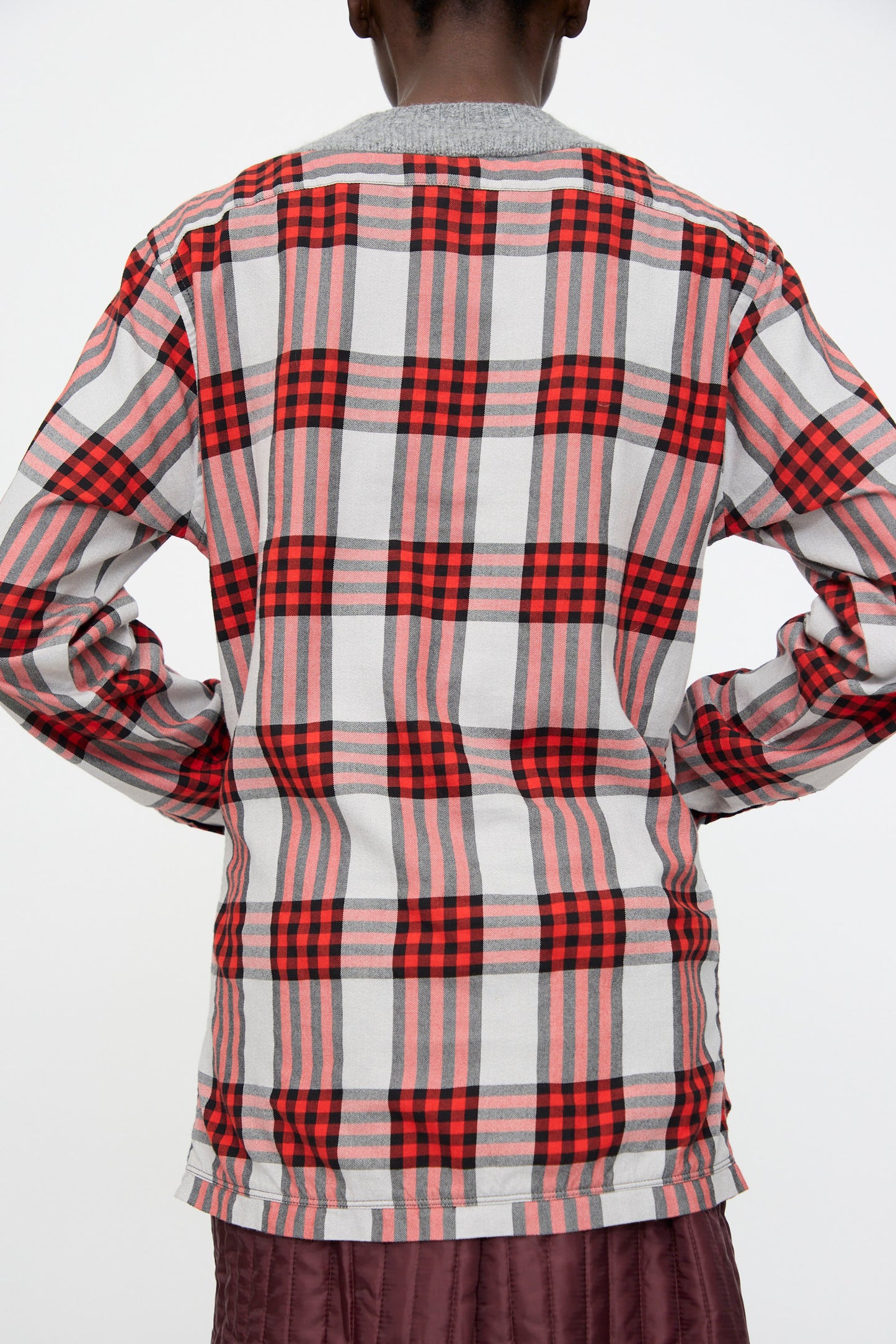 Model wearing the Bless No. 68 Frontinsertpullover in Unique II, a long-sleeve red and white plaid flannel shirt with a relaxed fit, shown from the back with hands on hips against a plain background.