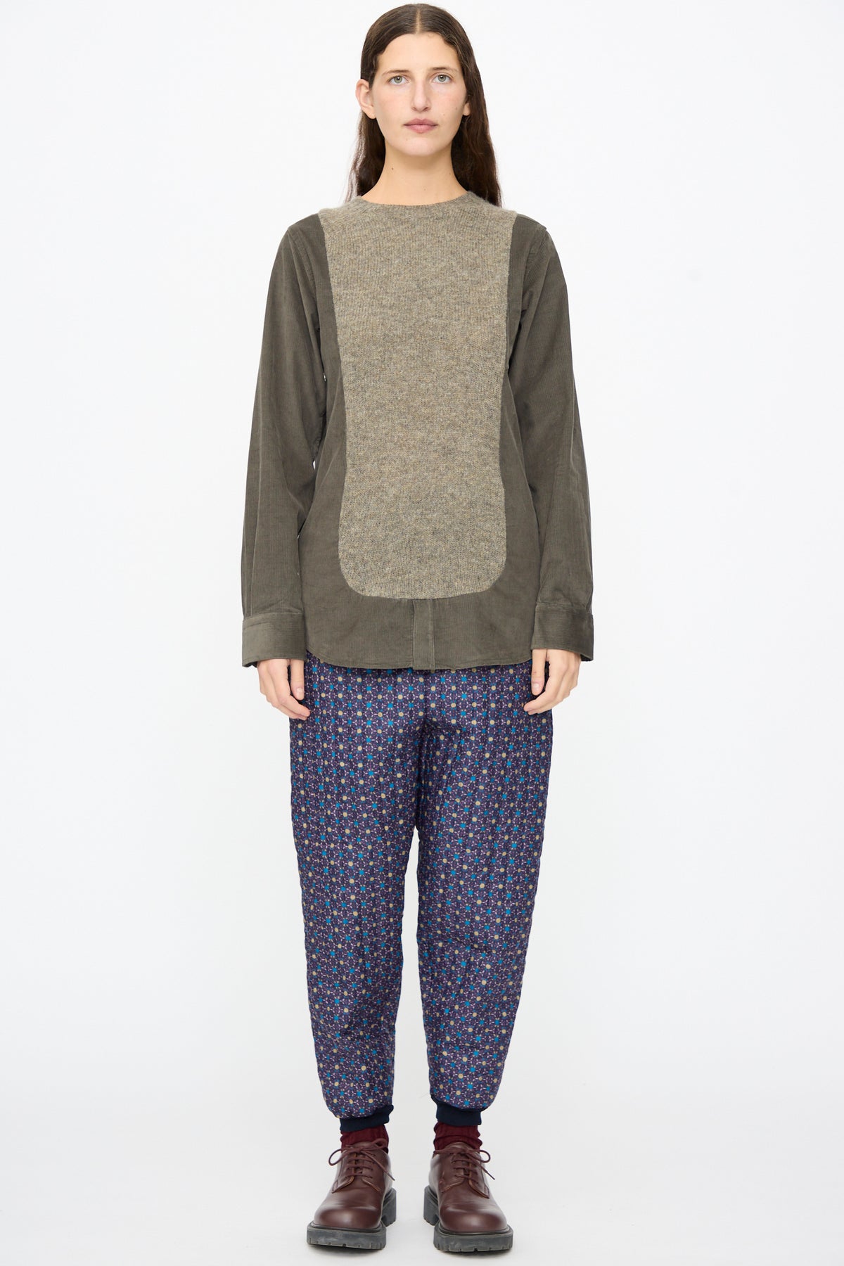 A person wearing a Bless No. 68 Frontinsertpullover in Unique III with a textured chest panel, patterned trousers, and brown shoes.