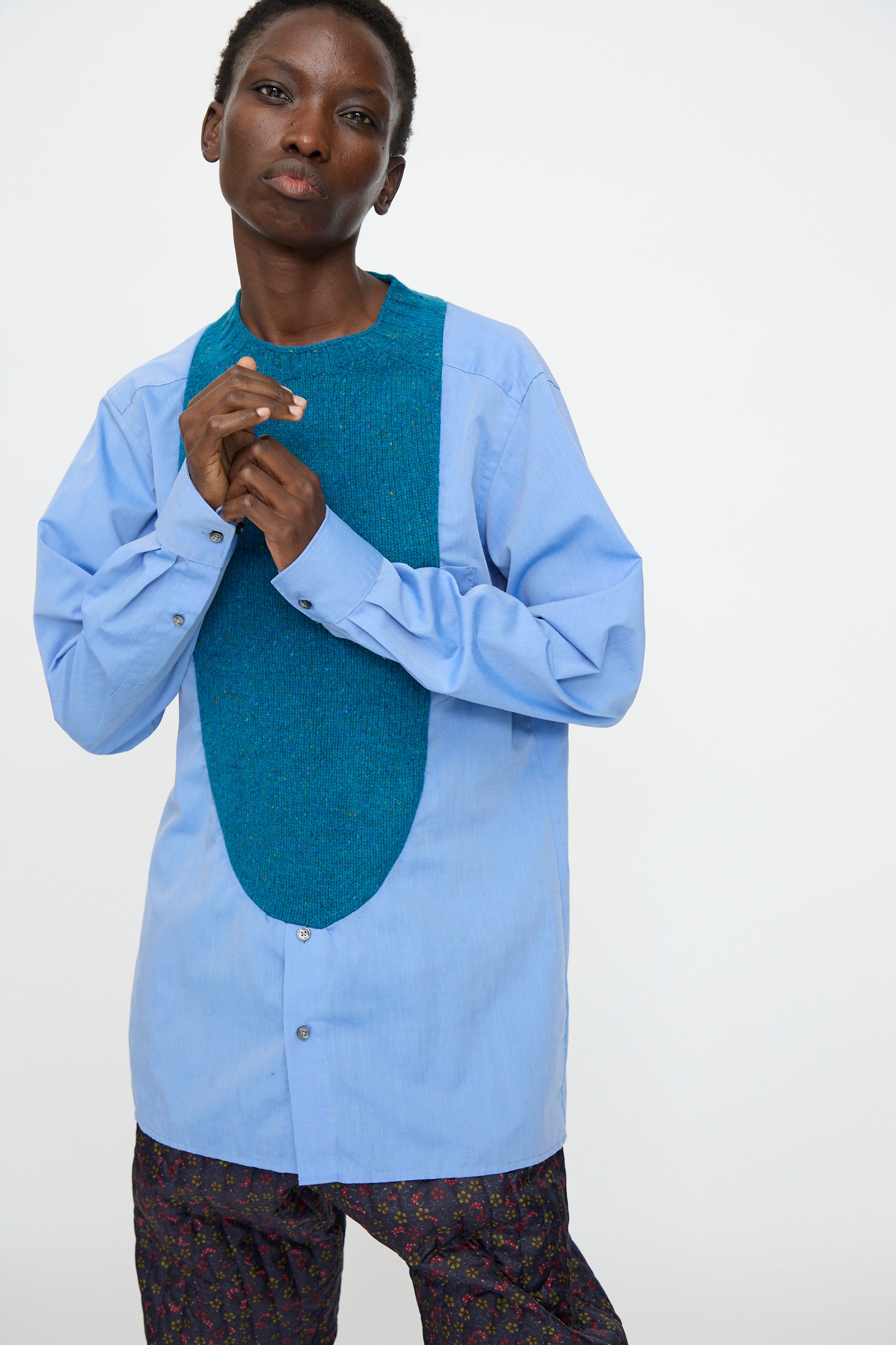 A person stands against a plain background wearing the Bless No. 68 Frontinsertpullover in Unique III paired with patterned dark trousers.