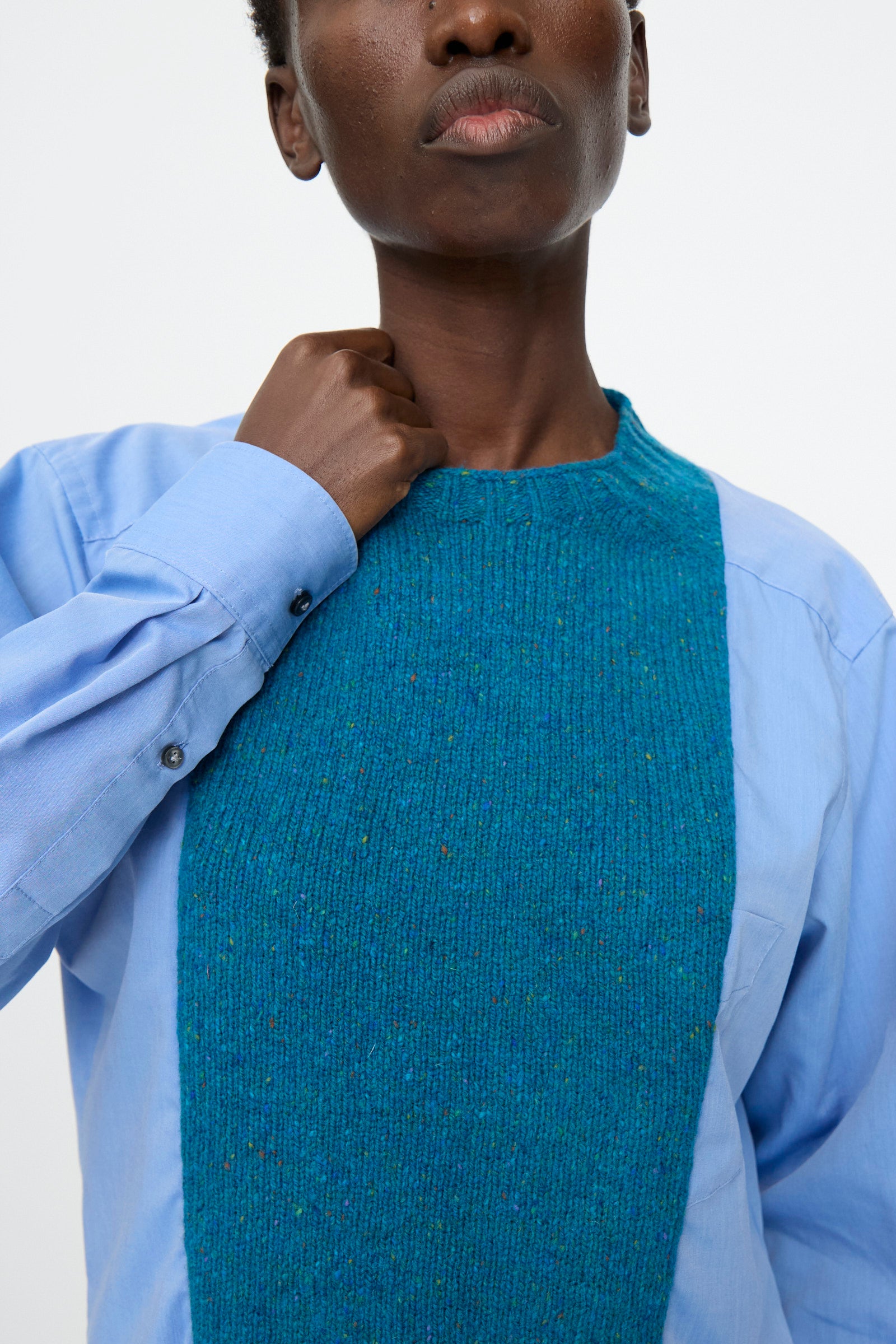 A person photographed from the shoulders up wears a relaxed fit light blue cotton poplin shirt with the Bless No. 68 Frontinsertpullover in Unique III, featuring a teal shetland wool panel, layered on top.