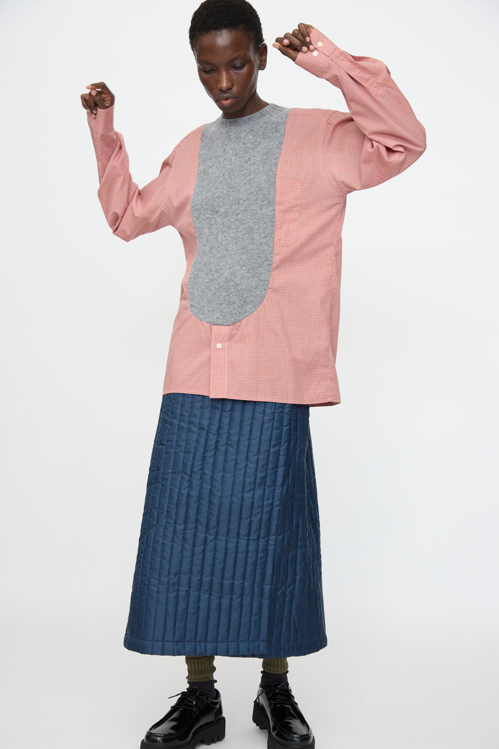 A person stands against a white background wearing the Bless No. 68 Frontinsertpullover in Unique IV, paired with a blue quilted skirt, dark shoes, and green socks.
