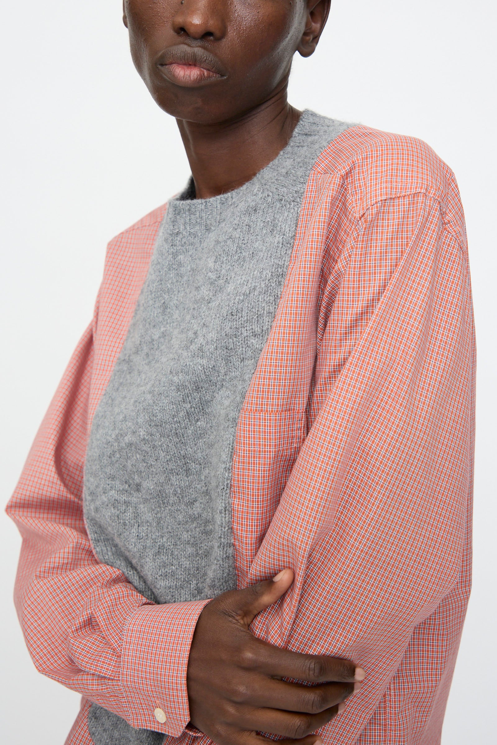 Model wearing Bless No. 68 Frontinsertpullover in Unique IV—a gray top layered under a red and white cotton poplin shirt, arms crossed with a neutral expression against a plain background.