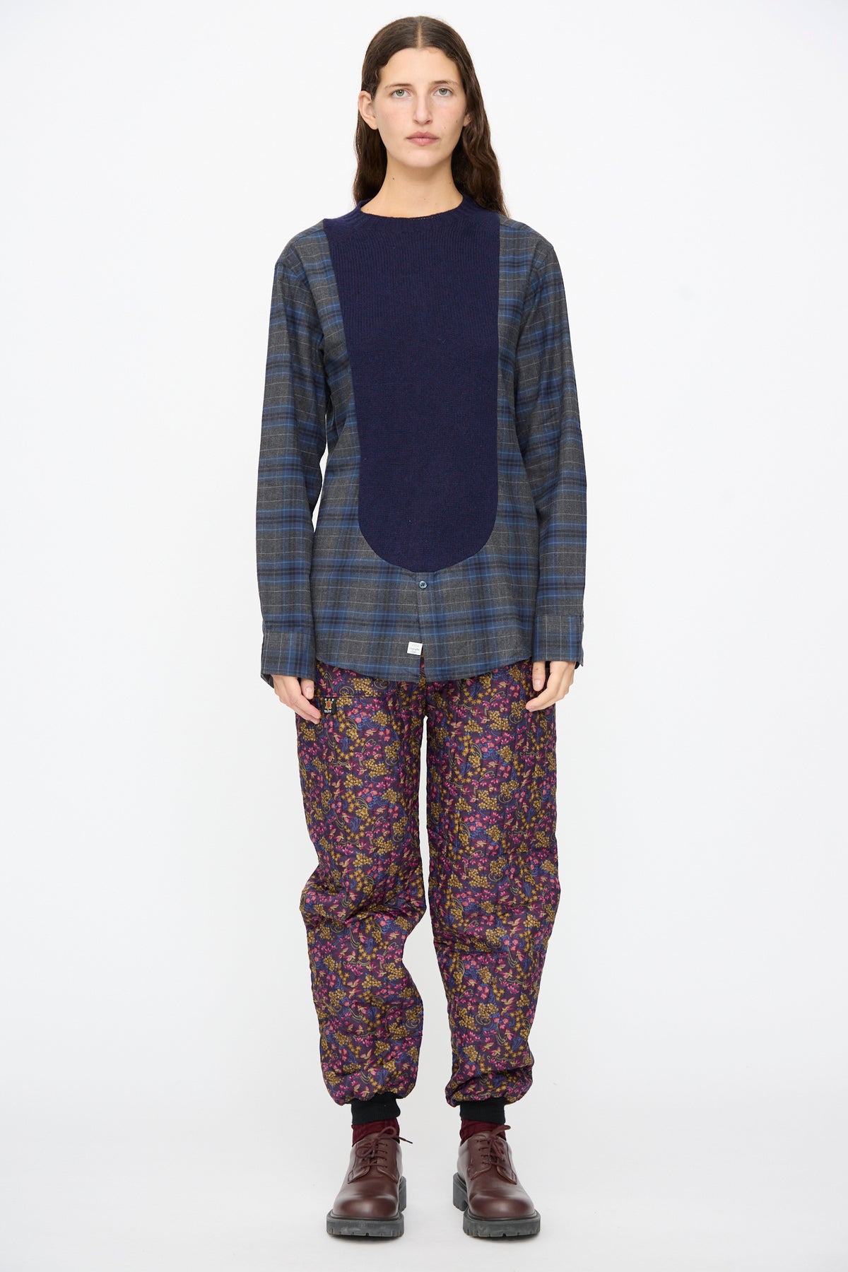 A model wears the Bless No. 68 Frontinsertpullover in Unique IV, featuring a navy-blue front panel and long sleeves, paired with dark floral-print trousers and brown lace-up shoes.