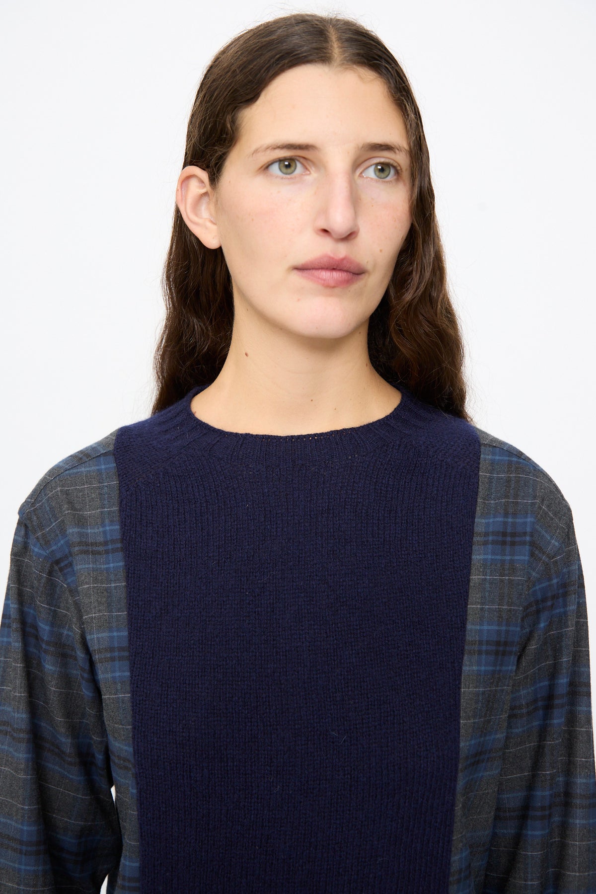 A woman wears the Bless No. 68 Frontinsertpullover in Unique IV, a shetland wool pullover featuring a dark blue knit center panel and plaid flannel shirt sleeves.