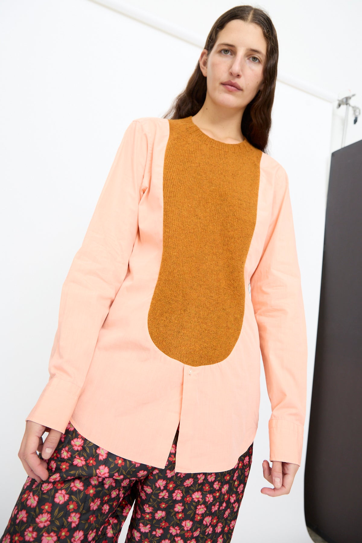 A person wears the Bless No. 68 Frontinsertpullover in Unique V, featuring a light peach button-down shirt with a Shetland wool knit front panel, paired with floral print trousers.