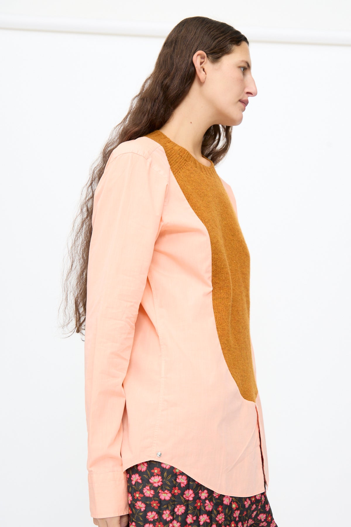 A person wears a Bless No. 68 Frontinsertpullover in Unique V, a long-sleeved light pink pullover featuring a contrasting brown knit panel on the front.