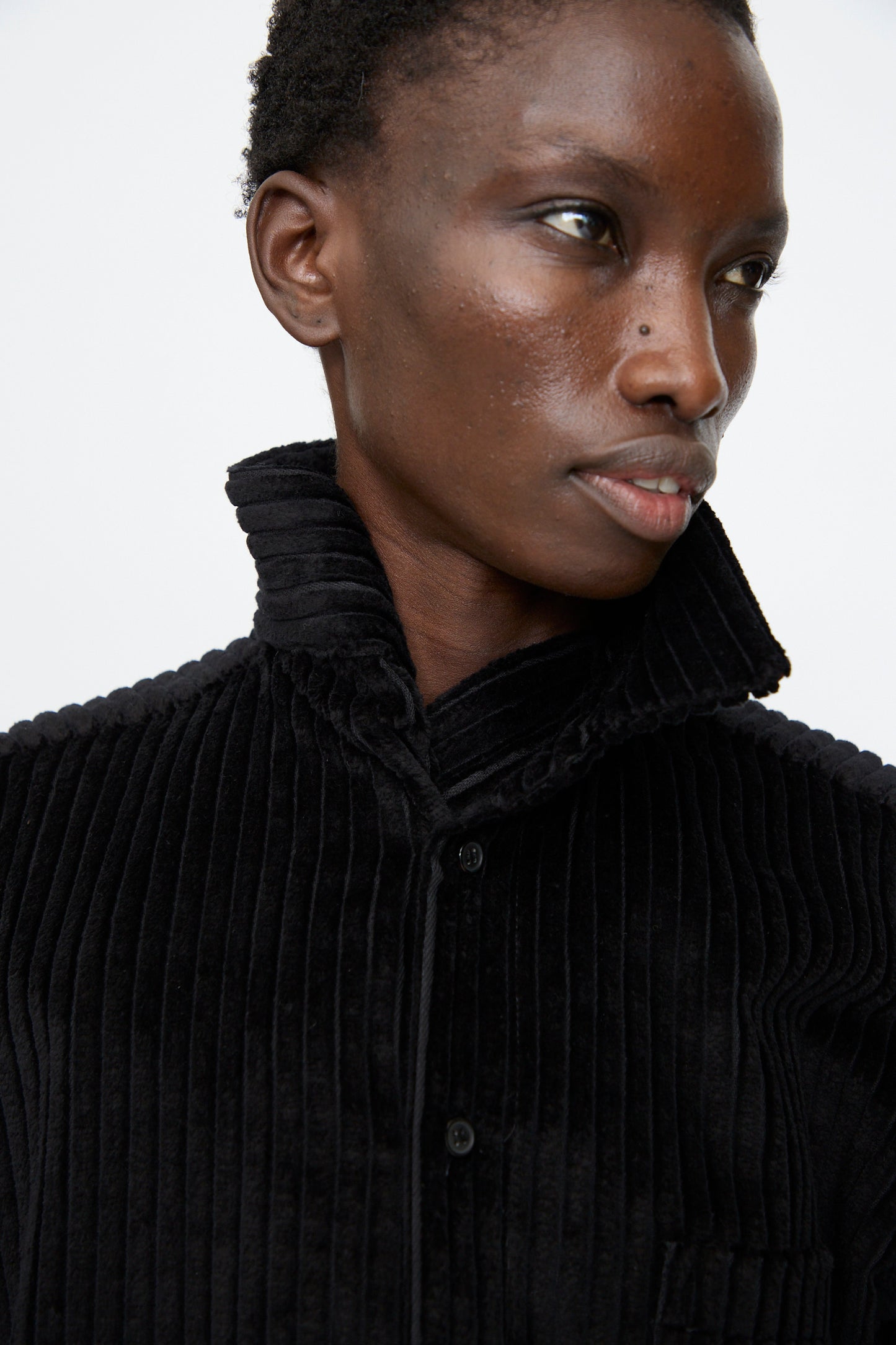 A person wearing the Bless No. 68 Neckerchiefer in black corduroy, featuring a high, wrap collar turned up, poses against a plain white background.
