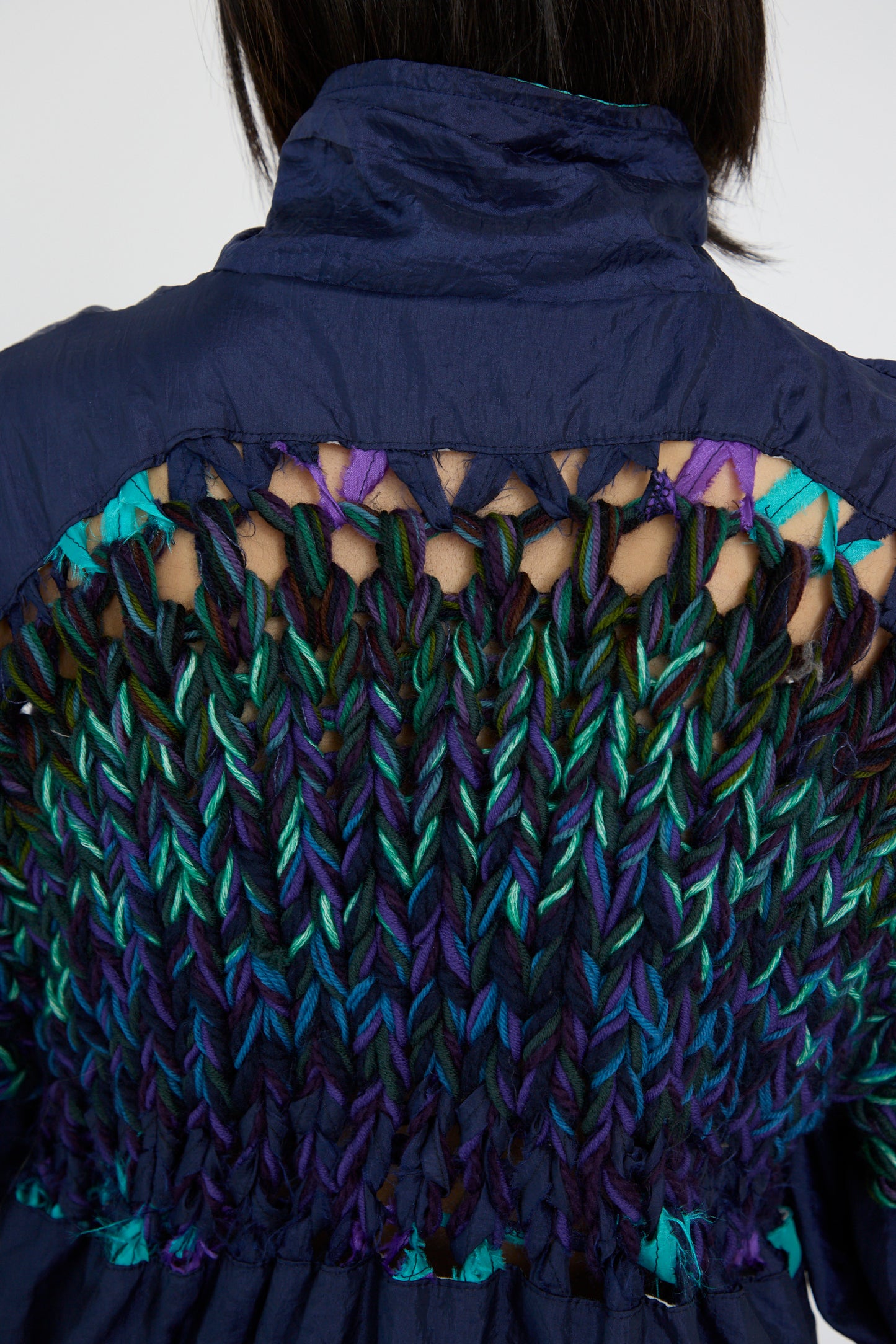 Back view of a person wearing the Bless No. 70 Aknitter Unique Jacket in Multicolor Mix II, featuring a vibrant design on the upper back with green, teal, and purple knitted yarn.