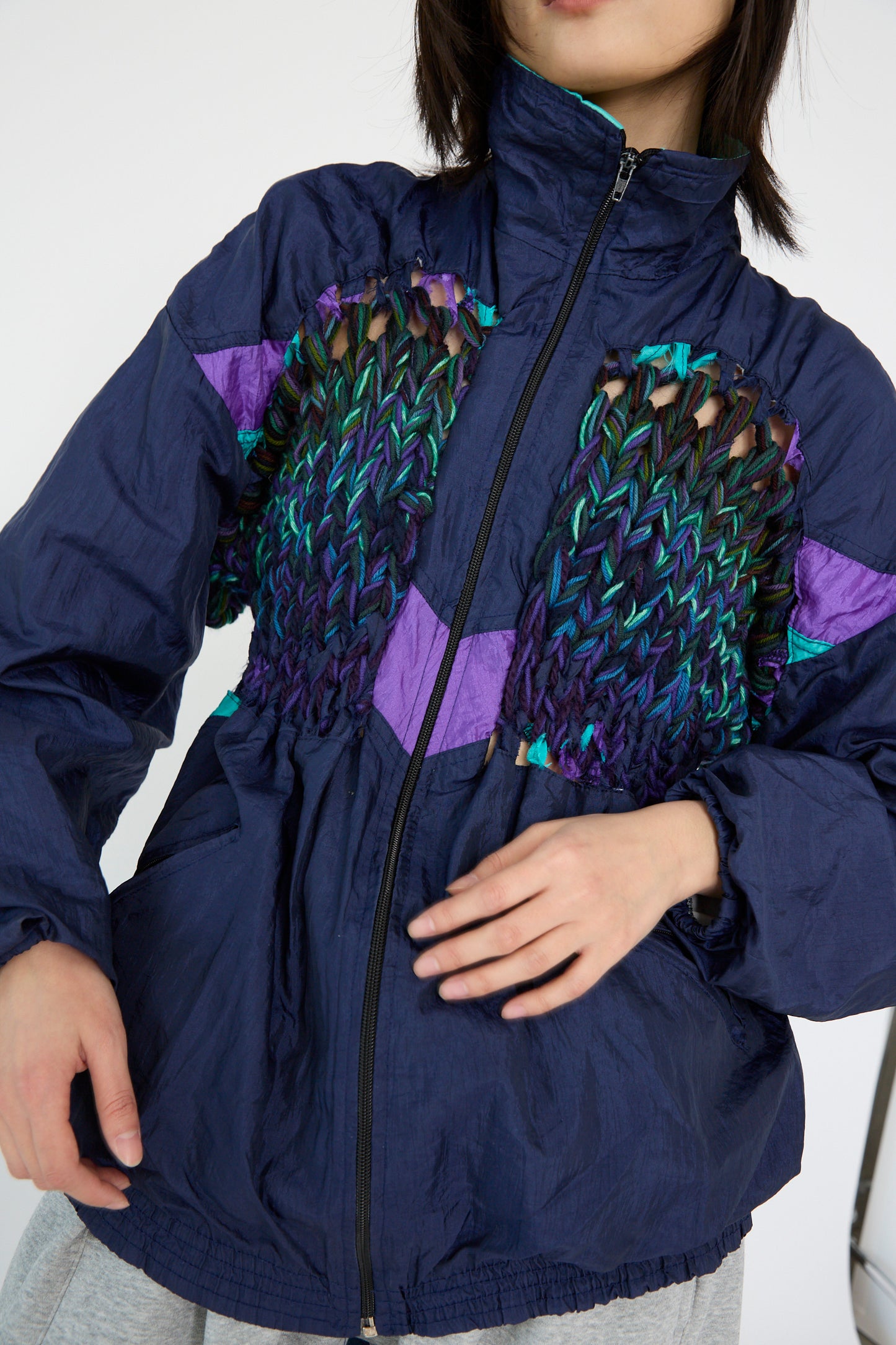 A person wearing the Bless No. 70 Aknitter Unique Jacket in Multicolor Mix II, featuring an intricate woven design and purple accents, against a plain background. 