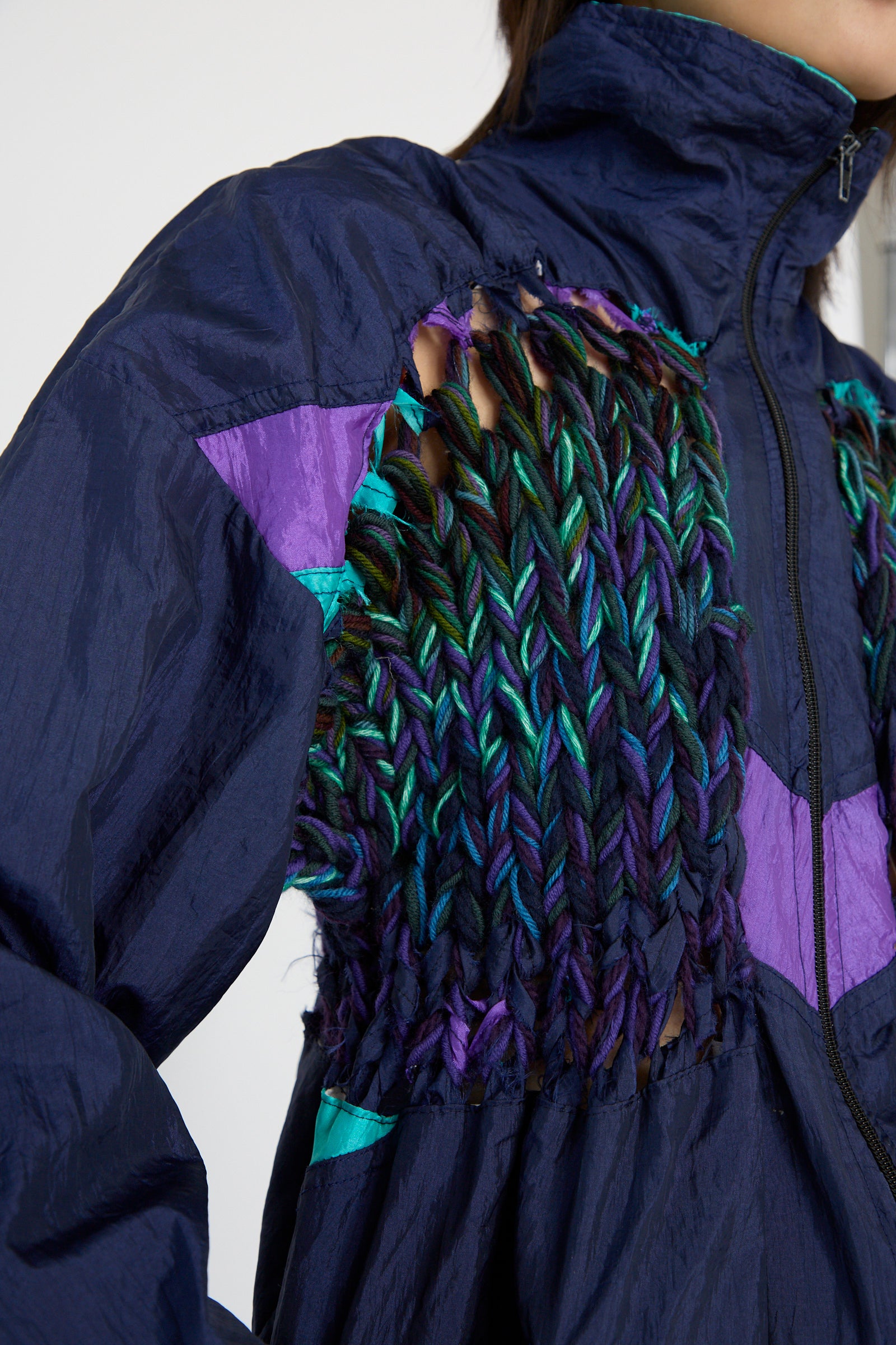 Close-up of the No. 70 Aknitter Unique Jacket in Multicolor Mix II by Bless, featuring a navy base with a woven, multi-color design accented in purple. The pattern incorporates textured threads in blue, green, and black for added depth.