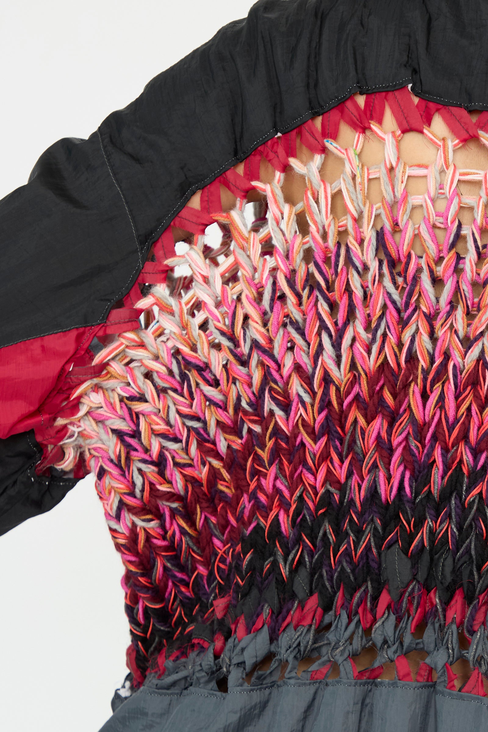 Close-up of the No. 70 Aknitter Unique Jacket by Bless, featuring an intricate multicolored woven design with red, pink, and gray threads on the back.