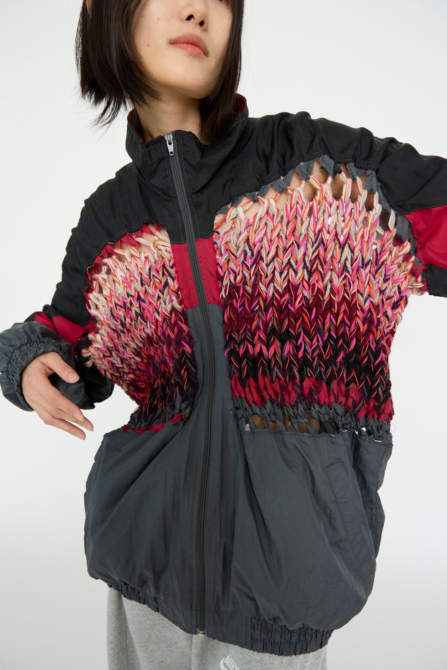 A model wearing the No. 70 Aknitter Unique Jacket in Multicolor Mix III by Bless, with vibrant knitted patterns and gray sections, against a white backdrop.