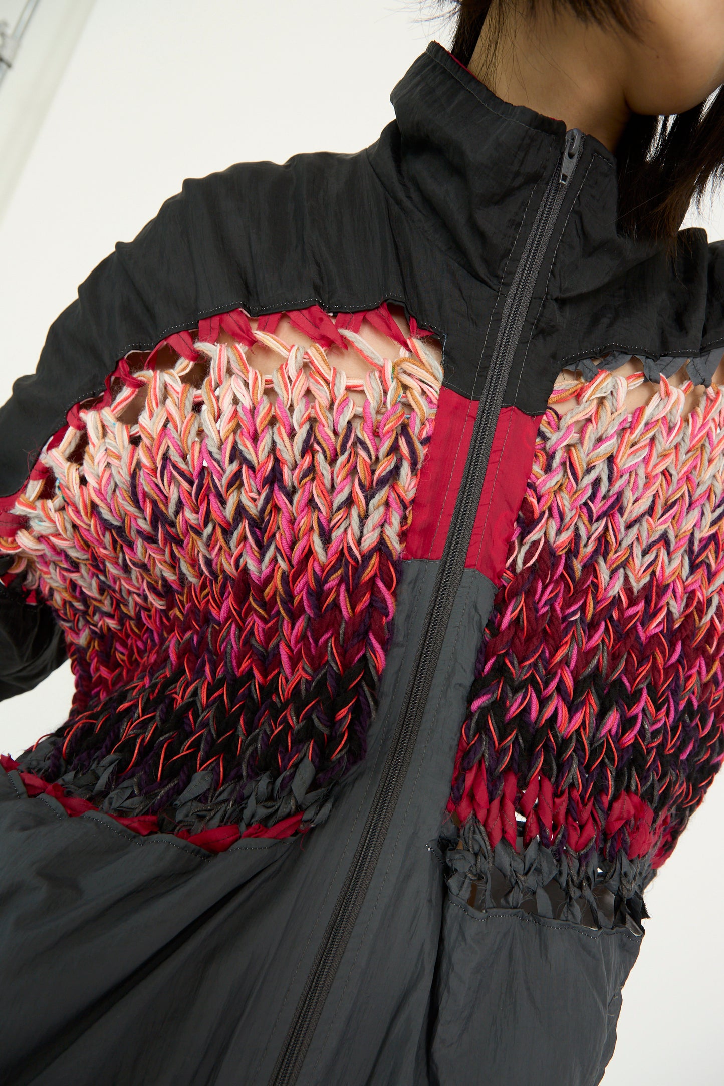 Close-up of Bless's No. 70 Aknitter Unique Jacket in Multicolor Mix III, featuring a woven pattern in red, pink, and black. It has a high collar and front zipper, on a model against a white background